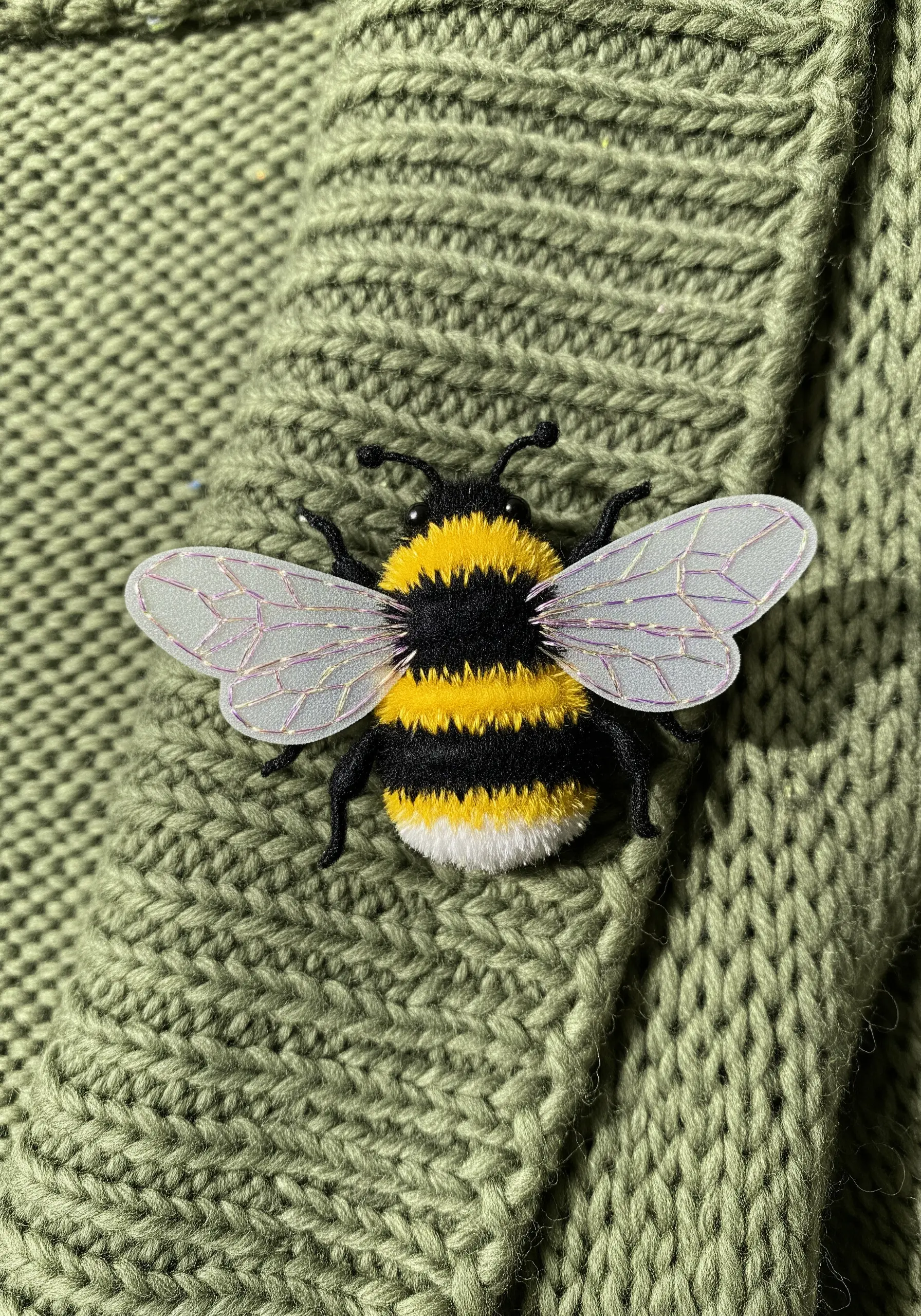 A three-dimensional embroidered bee brooch with organza wings pinned to a green sweater