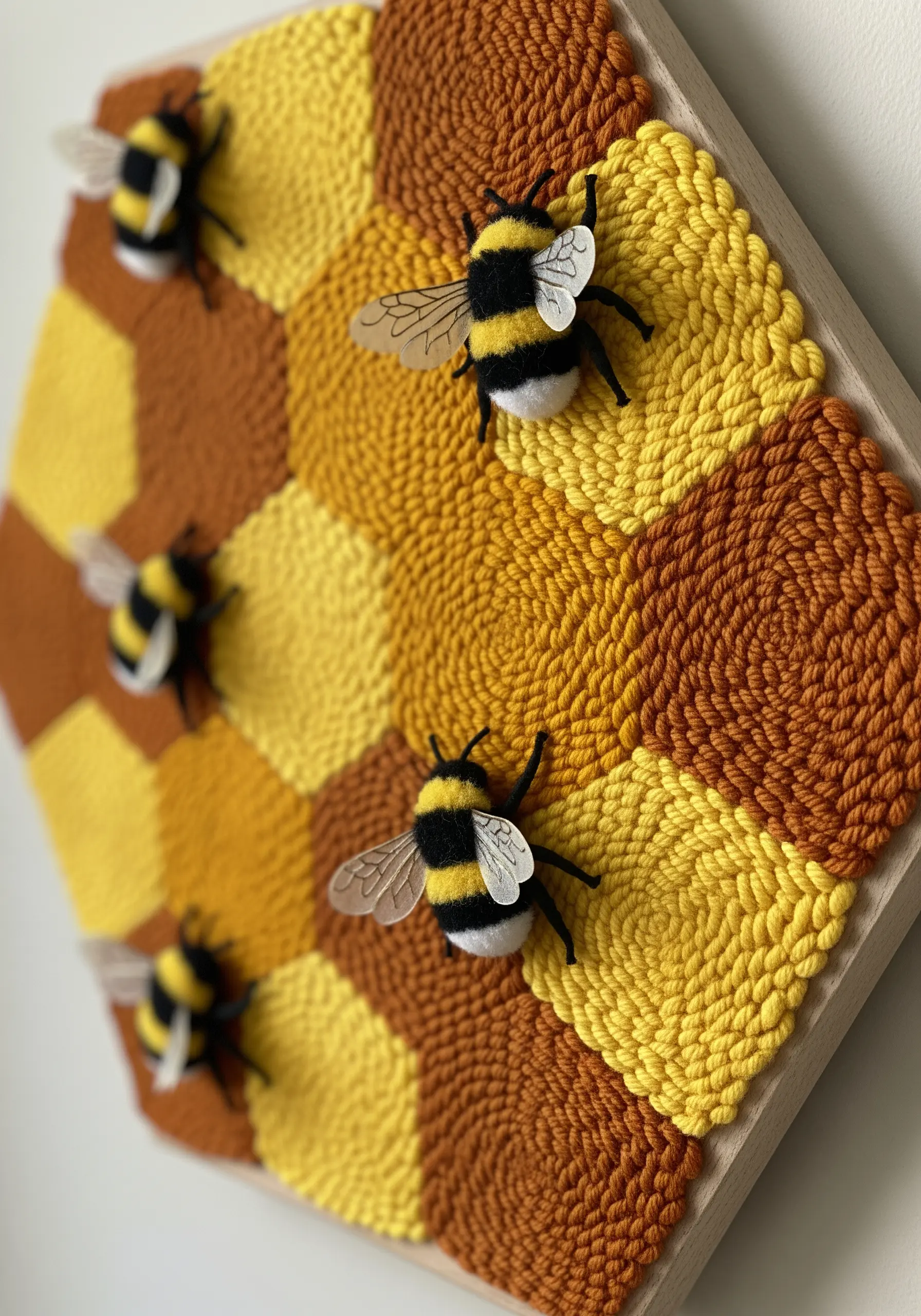 A hexagonal punch needle honeycomb with small, three-dimensional bees attached.