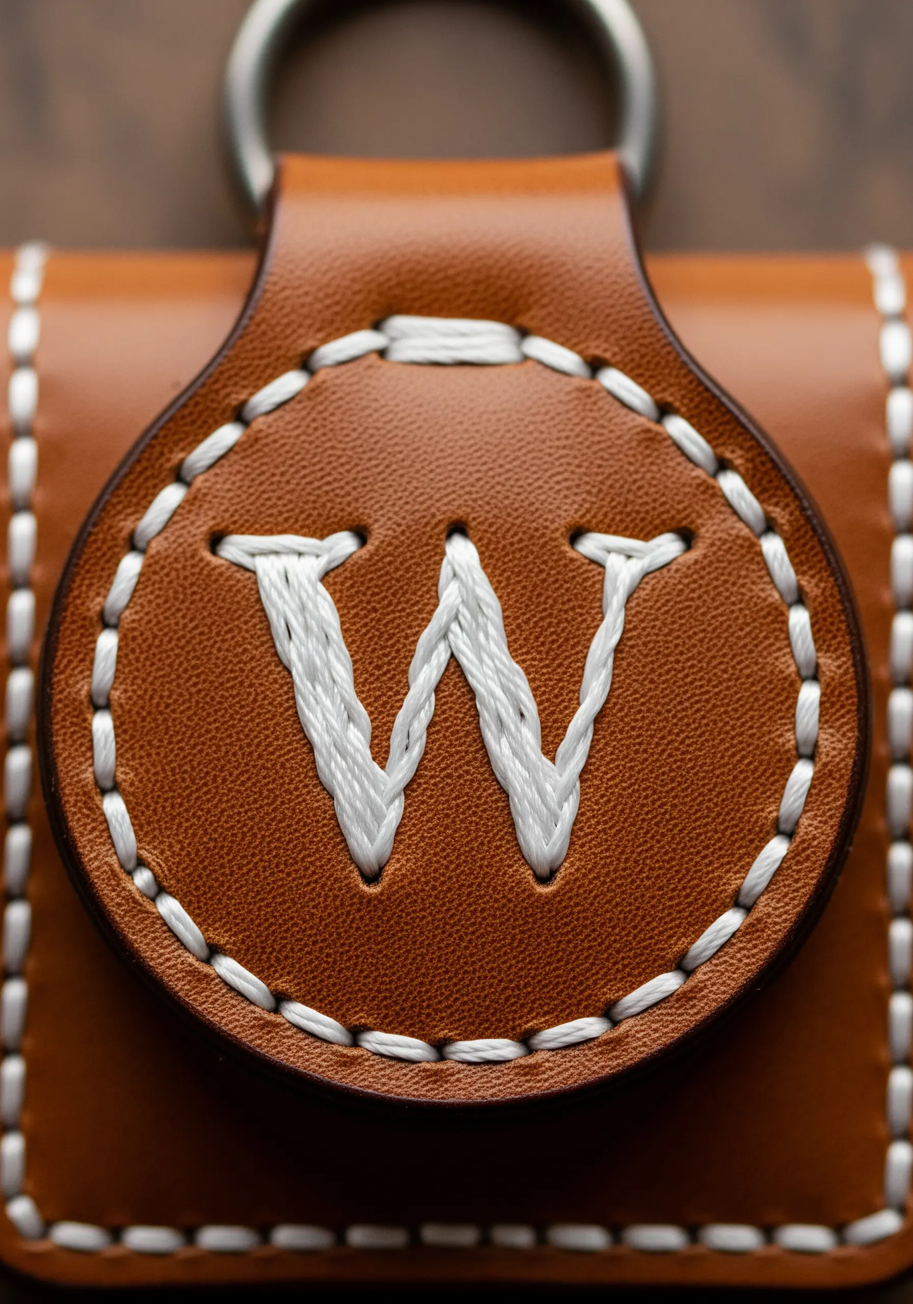 A bold white initial 'W' hand-stitched on a round brown leather tag.