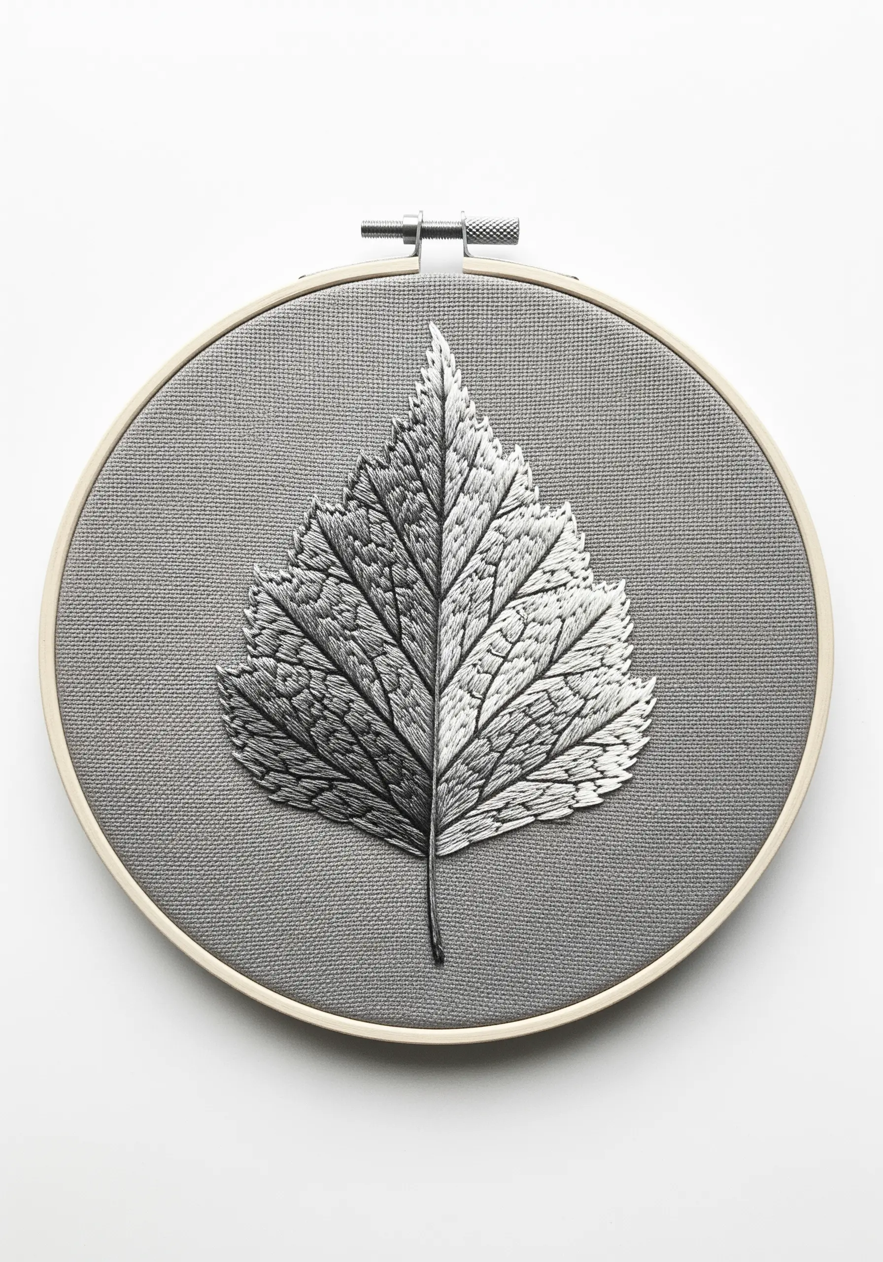 A leaf embroidered in monochrome, with one half in light shades and the other in dark shades.