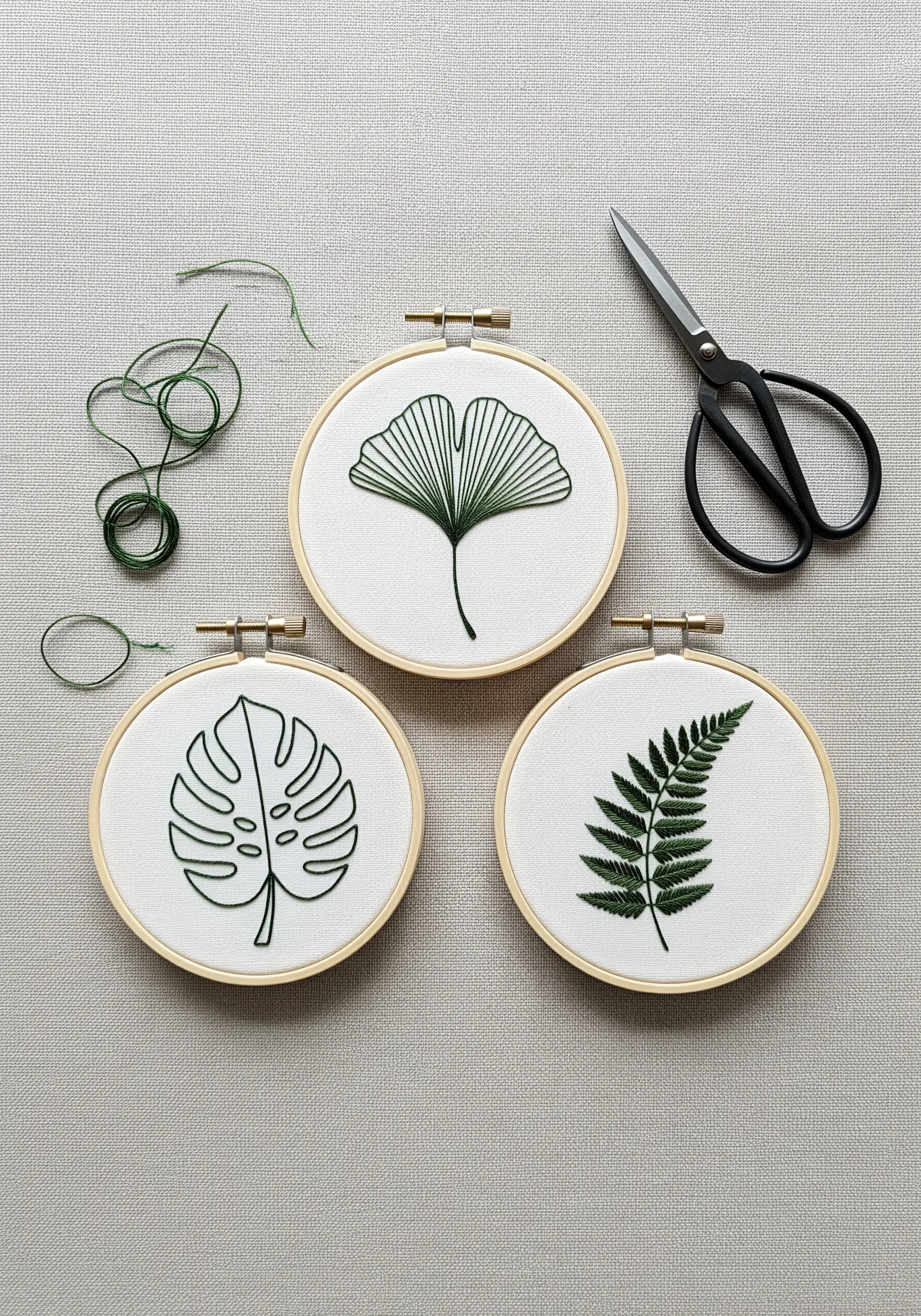 Three small embroidery hoops featuring minimalist green outlines of different leaves.