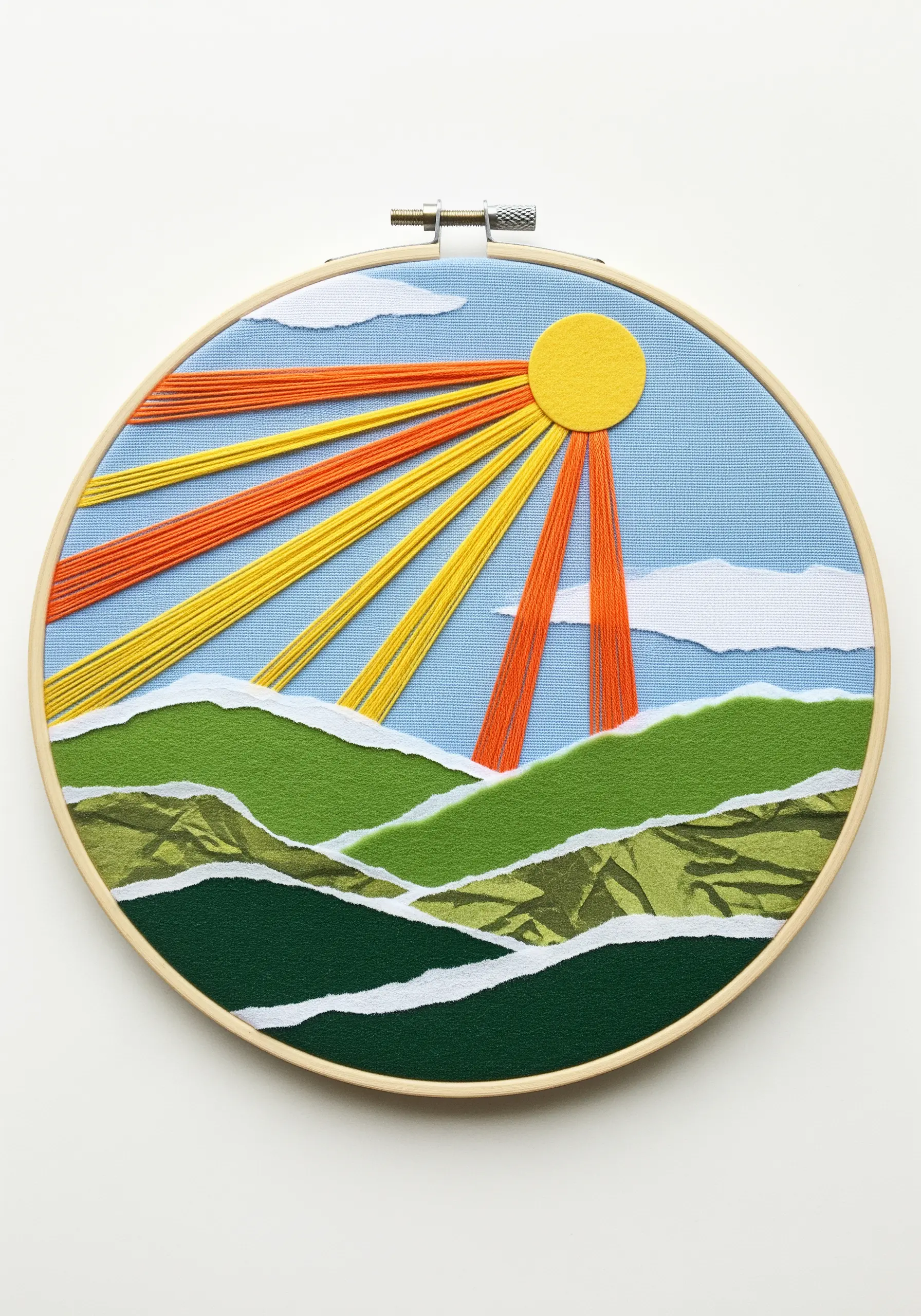 Embroidery hoop art with a landscape of torn paper hills and long stitched sun rays.