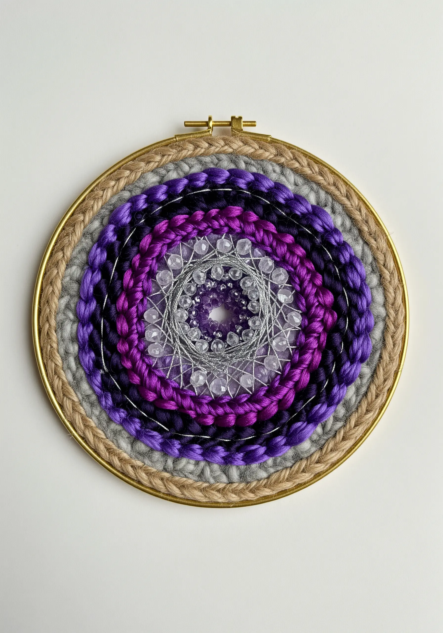 Woven mandala in a gold hoop with purple and grey yarn, featuring a crystal center.