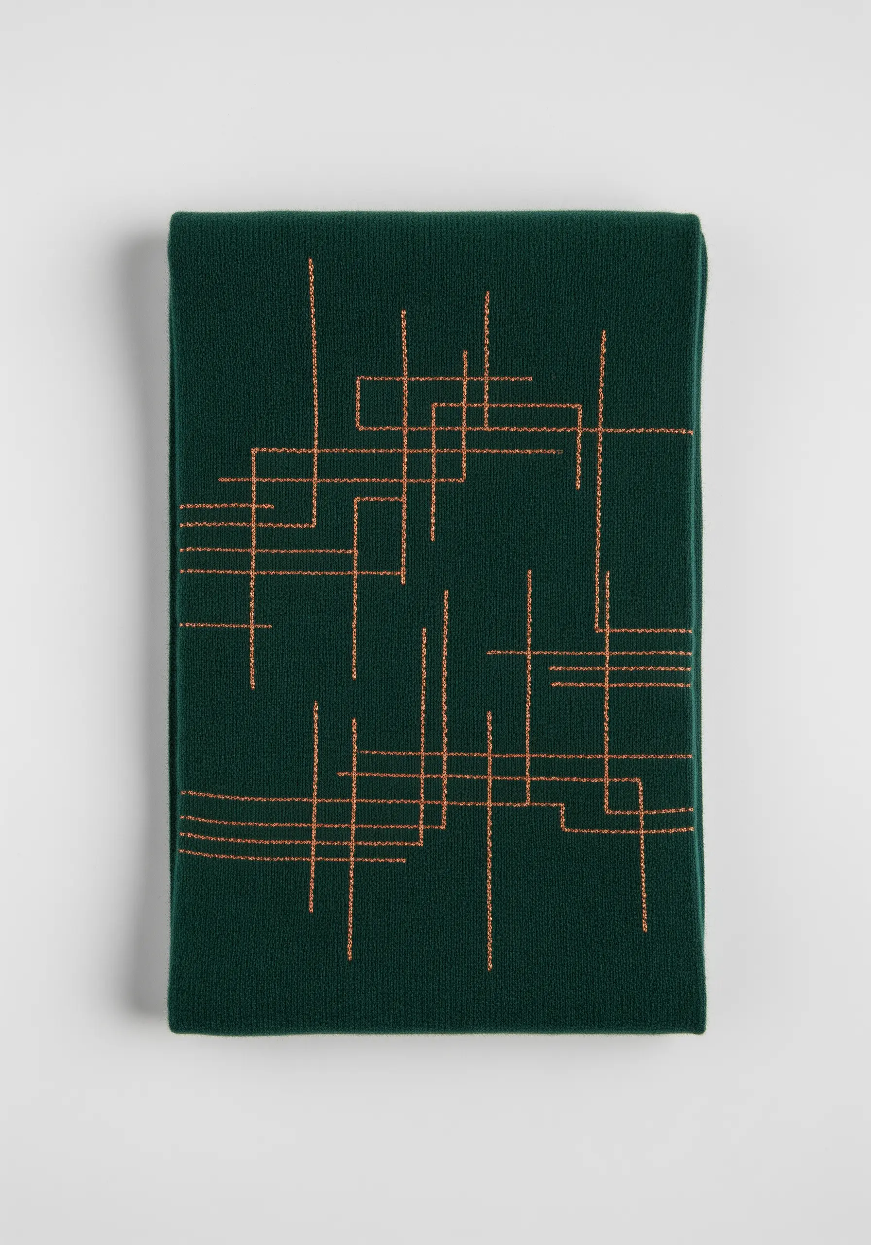 An abstract pattern of intersecting gold lines on a dark green knit scarf.