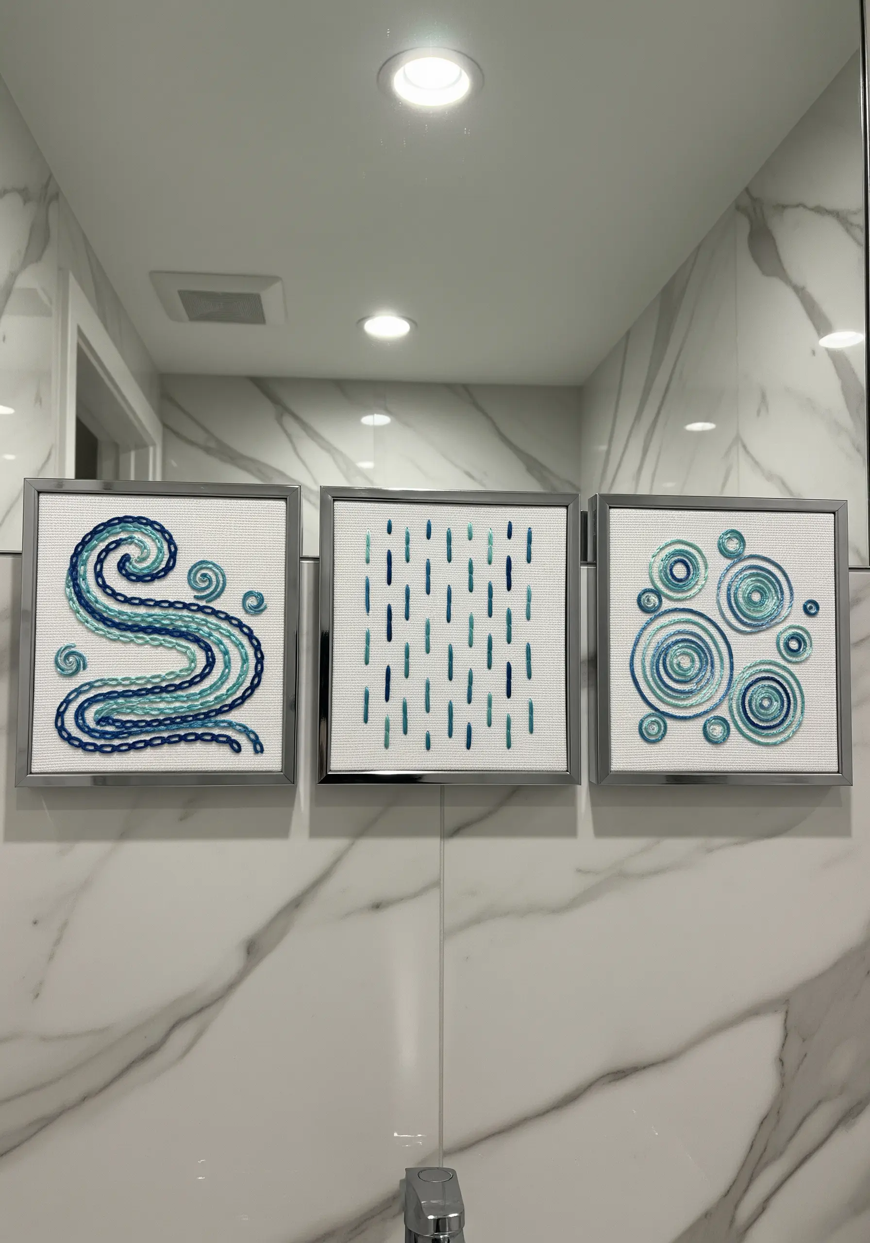 A triptych of small, framed abstract embroideries with a water theme in shades of blue.