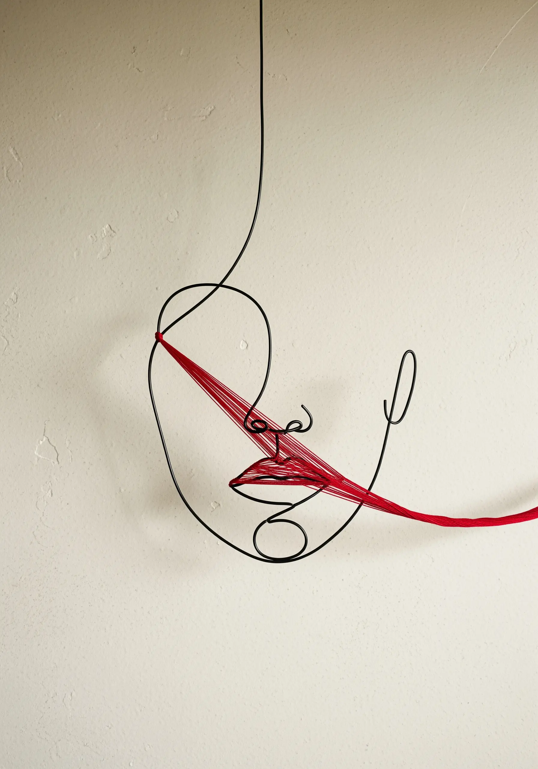 A minimalist face sculpted from black wire, with vibrant red thread stretched across the lips.