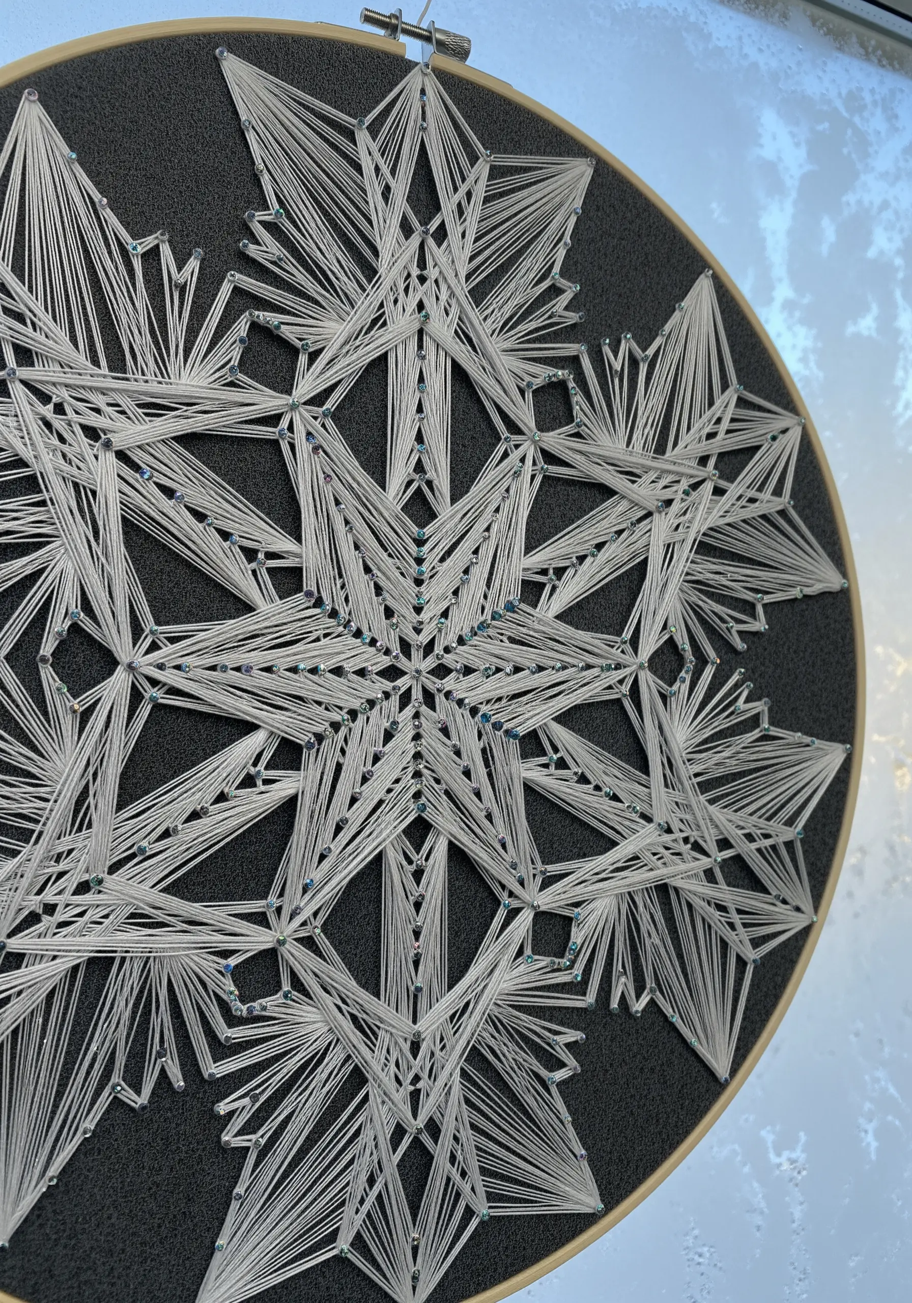 Intricate white string art snowflake with blue seed beads on dark gray fabric.