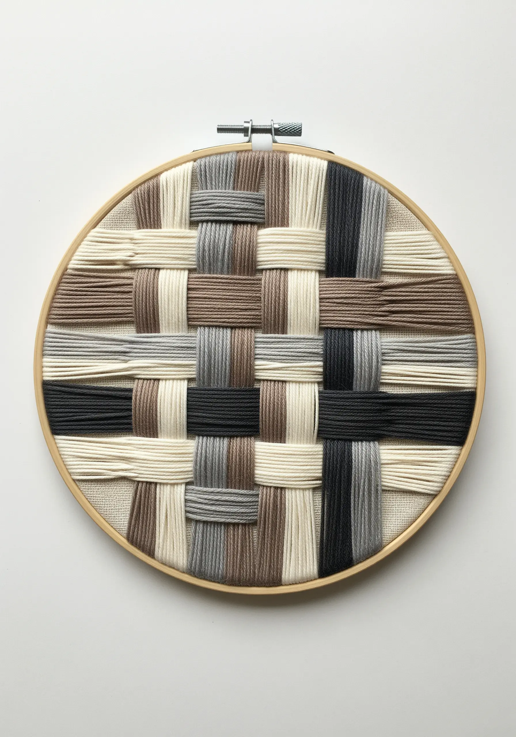 A close-up of thick yarns in neutral colors woven in a simple checkerboard pattern inside a hoop.