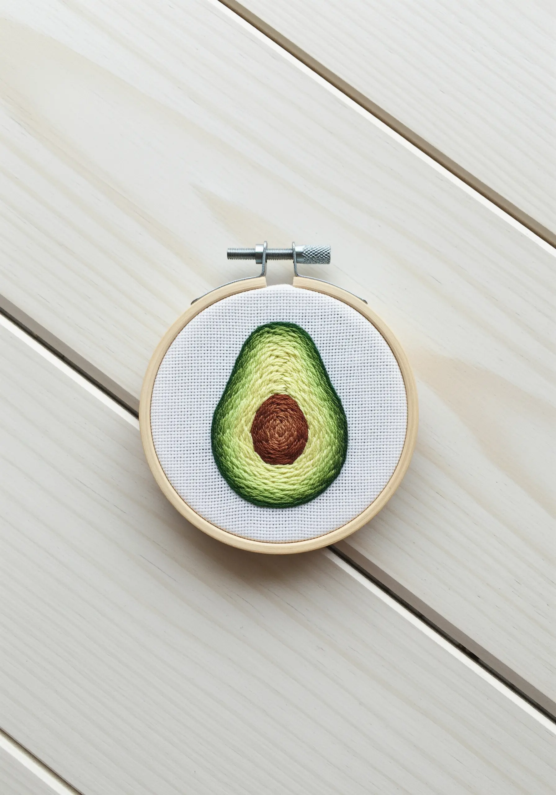 A small embroidered avocado half showing a smooth color gradient from green to yellow.