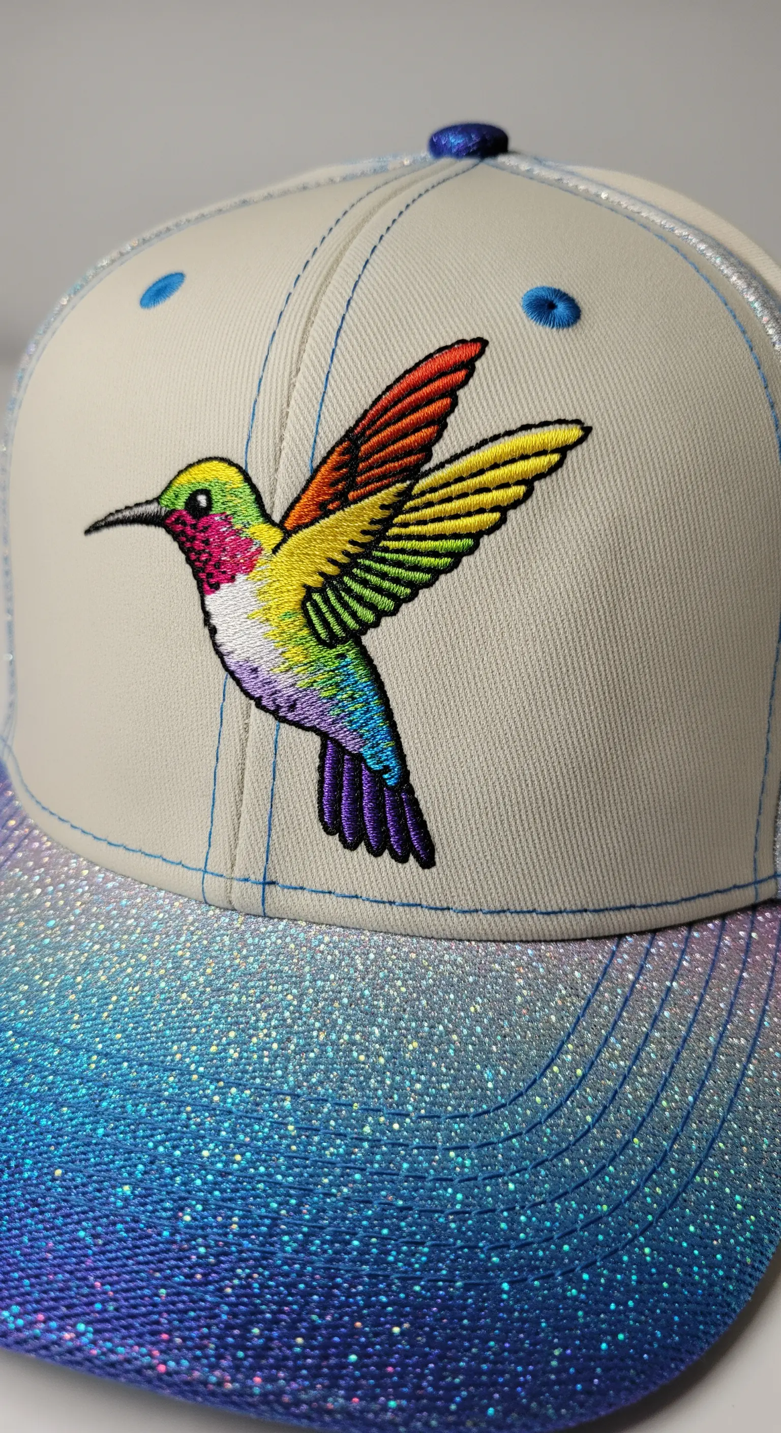 A machine-embroidered rainbow hummingbird on the front of a baseball cap.