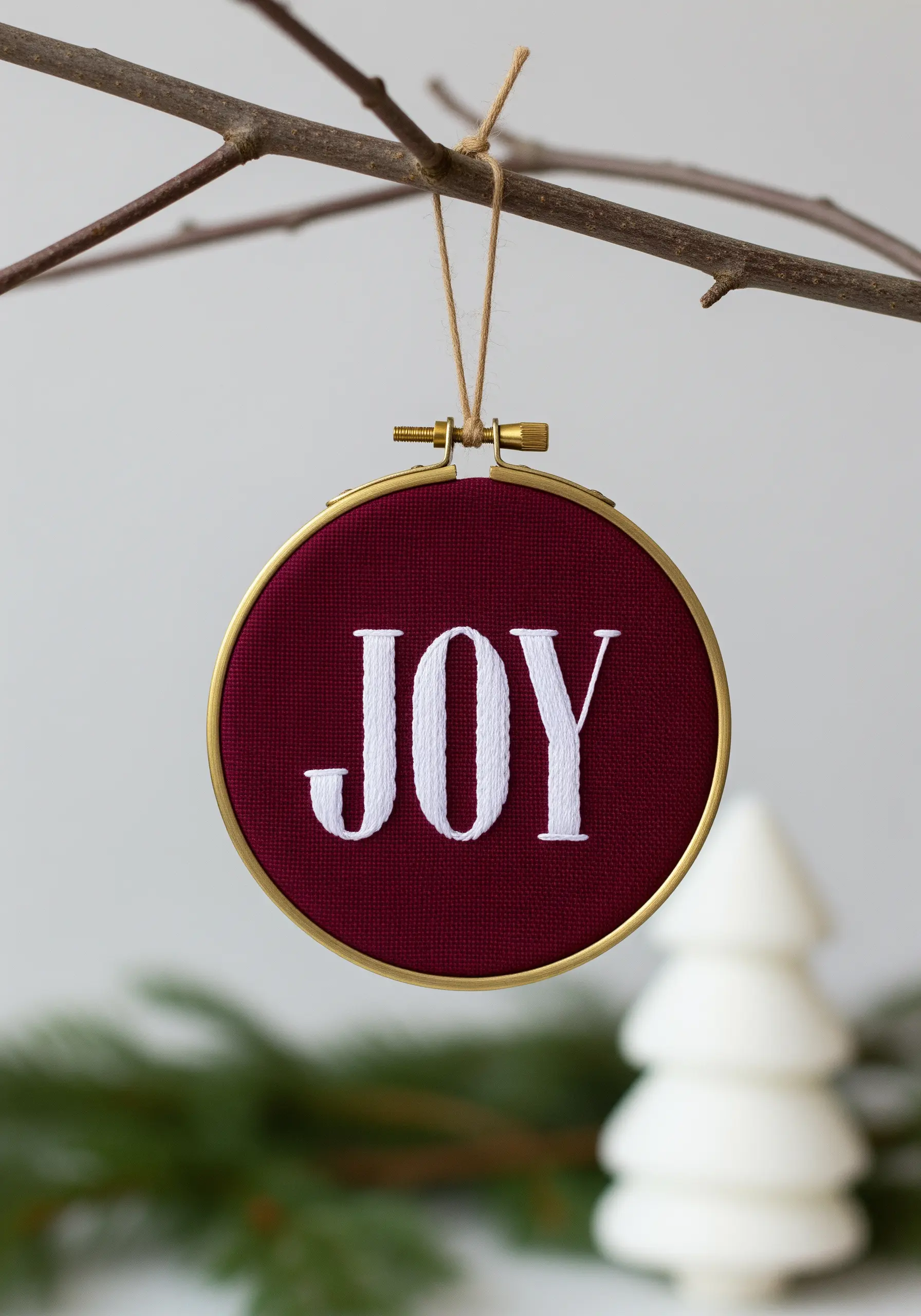 The word 'JOY' in white serif font, embroidered with satin stitch on burgundy fabric.