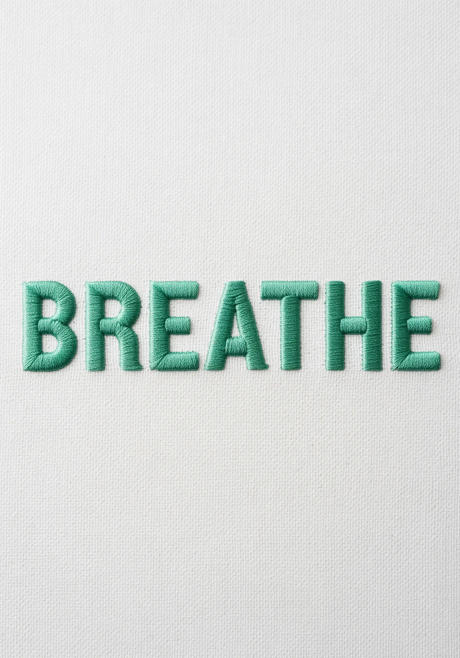 The word 'BREATHE' embroidered in a perfect green satin stitch on white canvas.