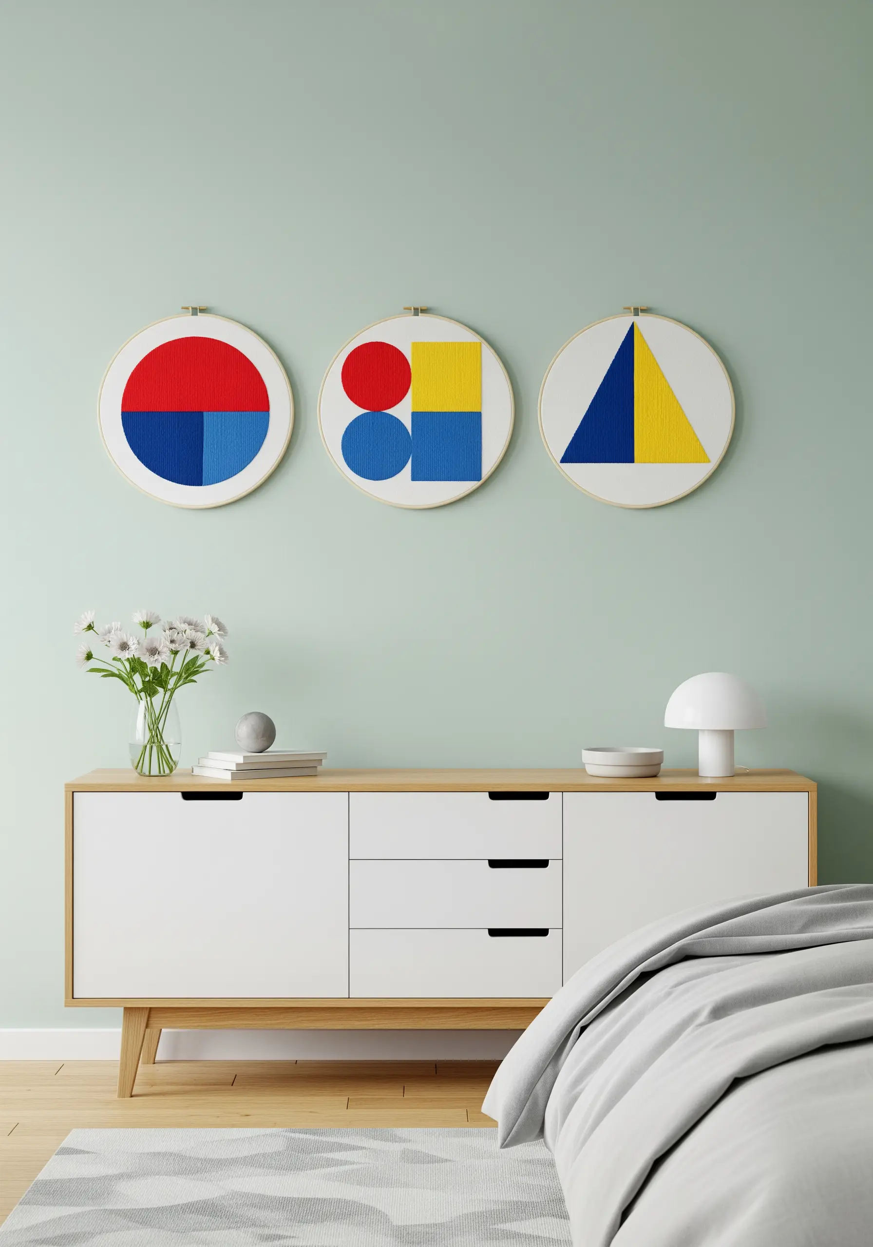 A trio of embroidery hoops with bold, minimalist geometric designs in red, blue, and yellow.