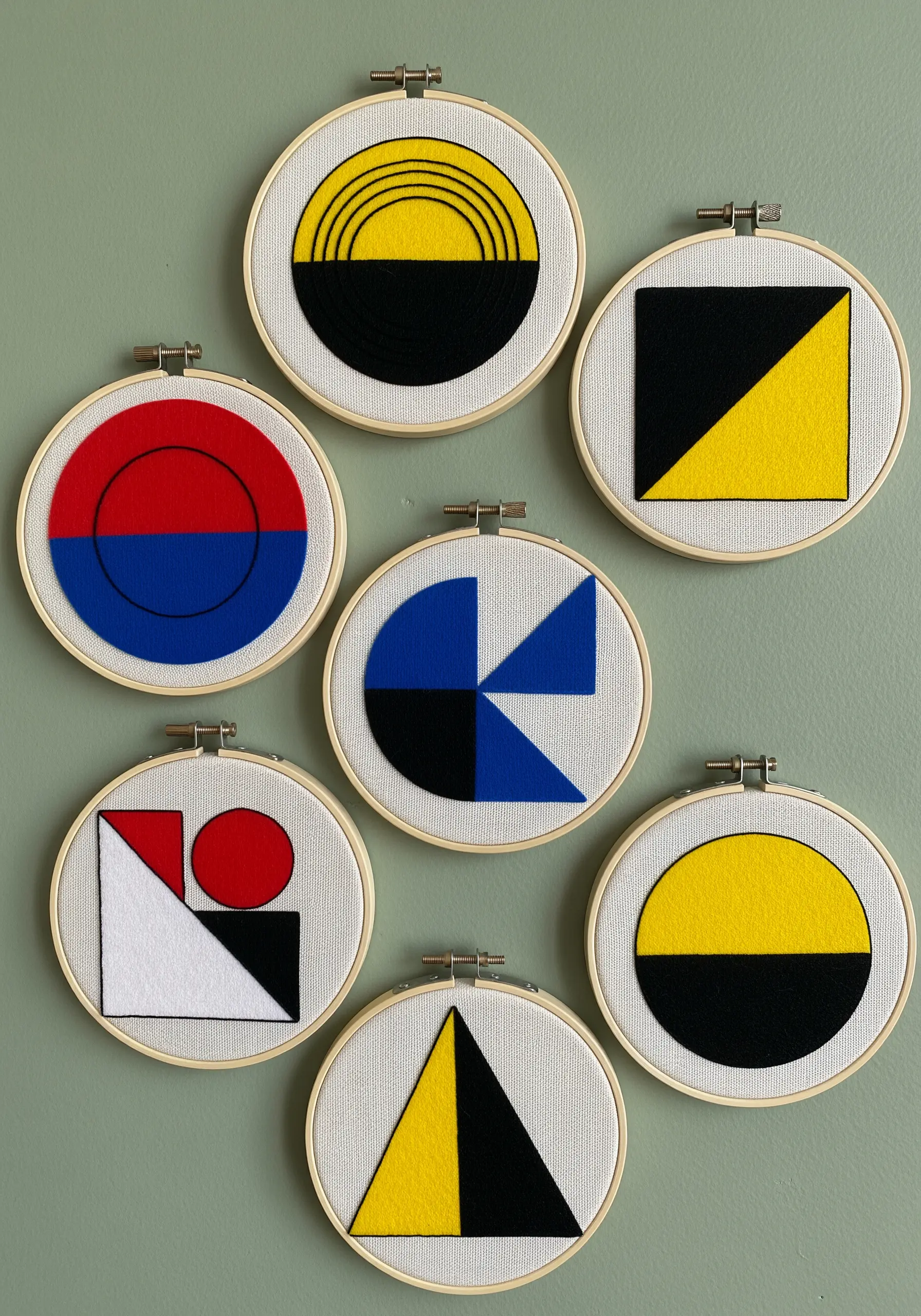A collection of small embroidery hoops with bold, geometric felt appliqué in primary colors.