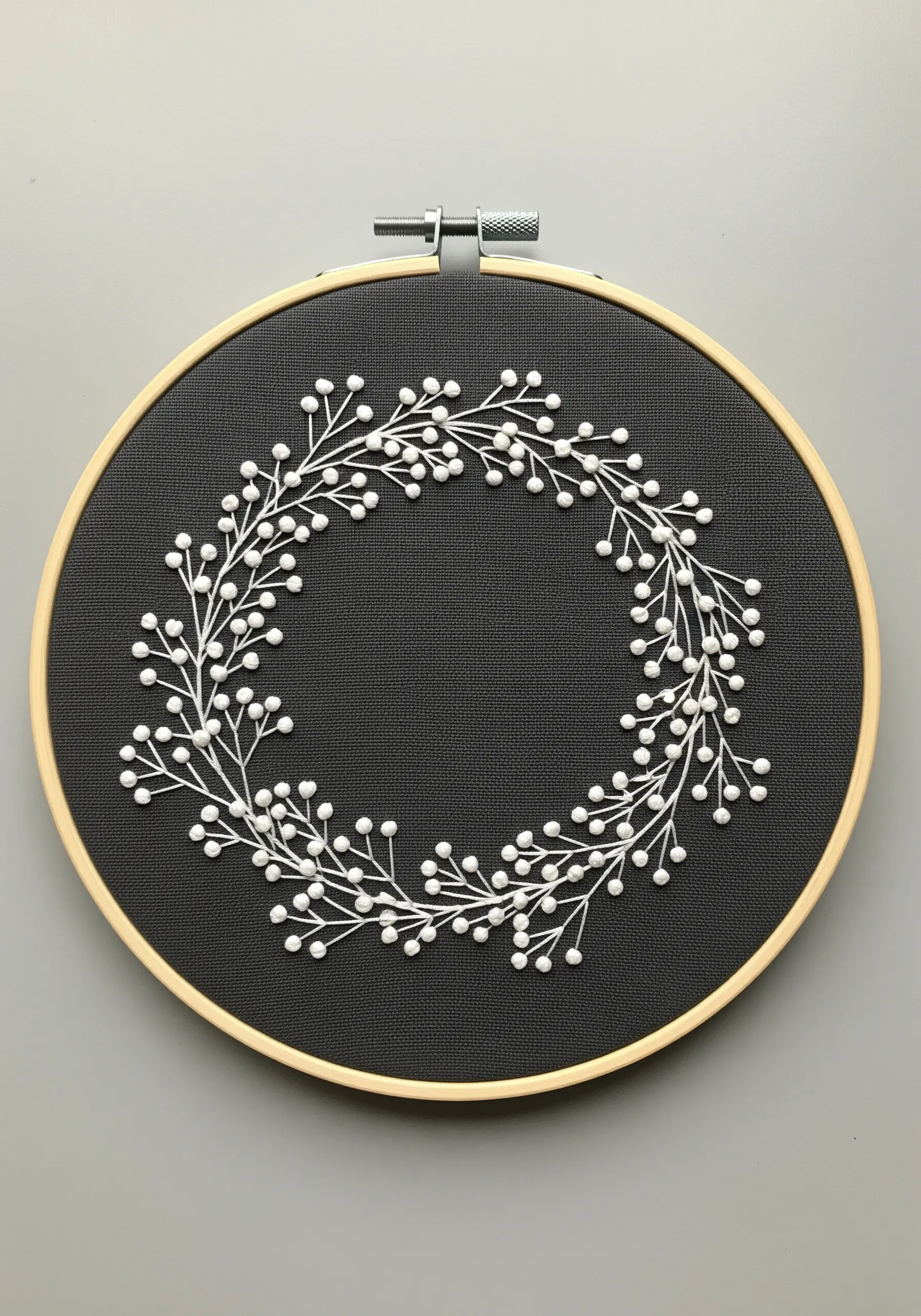 A delicate white baby's breath wreath embroidered with French knots on black fabric.