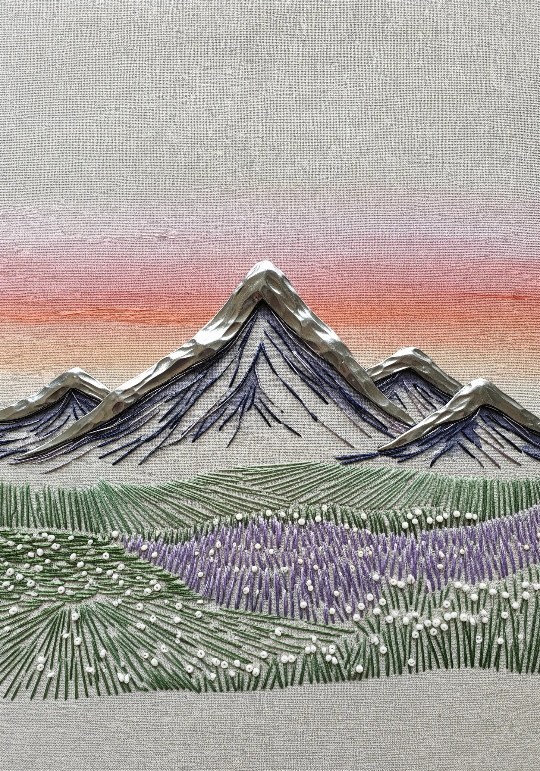 Embroidered mountain landscape with silver metallic fabric on the peaks and a painted sky.