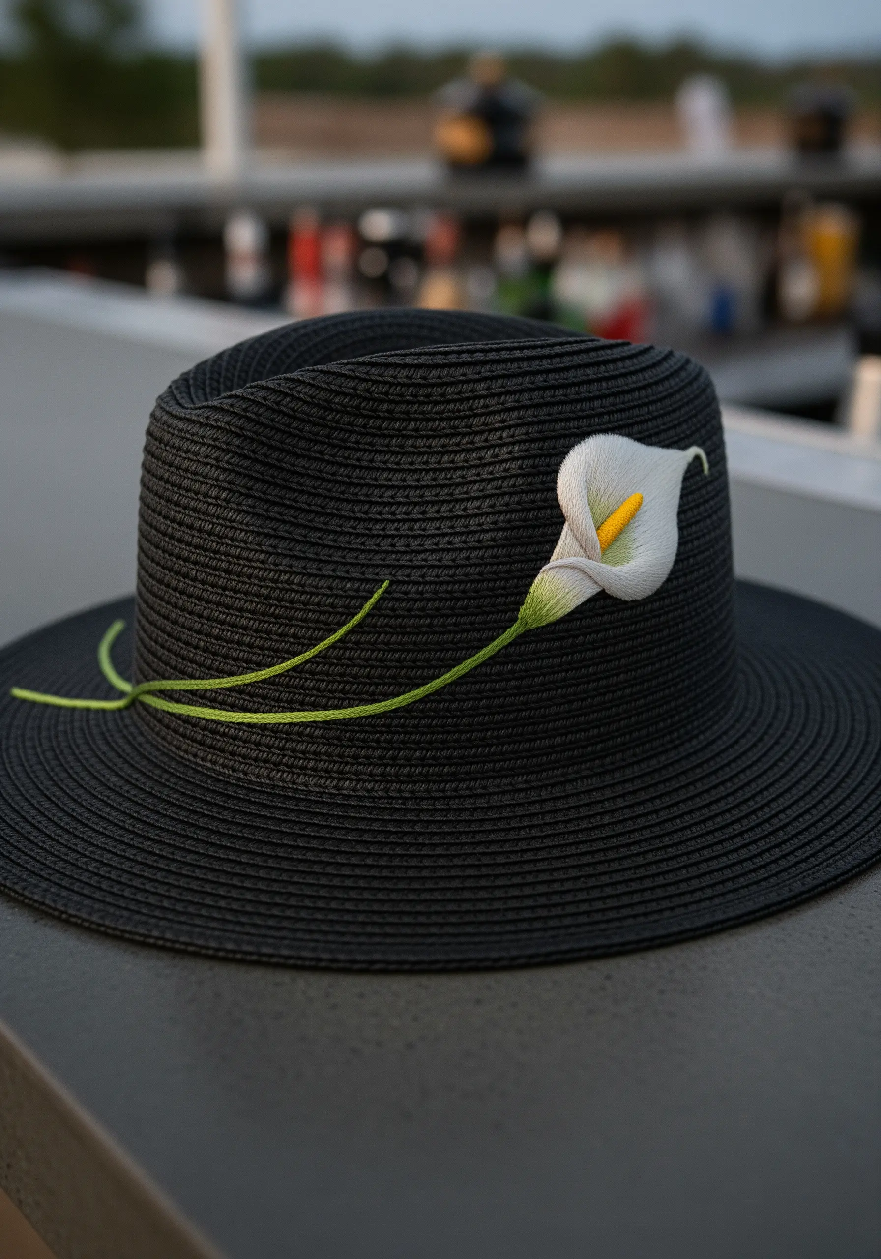 A single, three-dimensional white calla lily with a long green stem embroidered on a black hat.