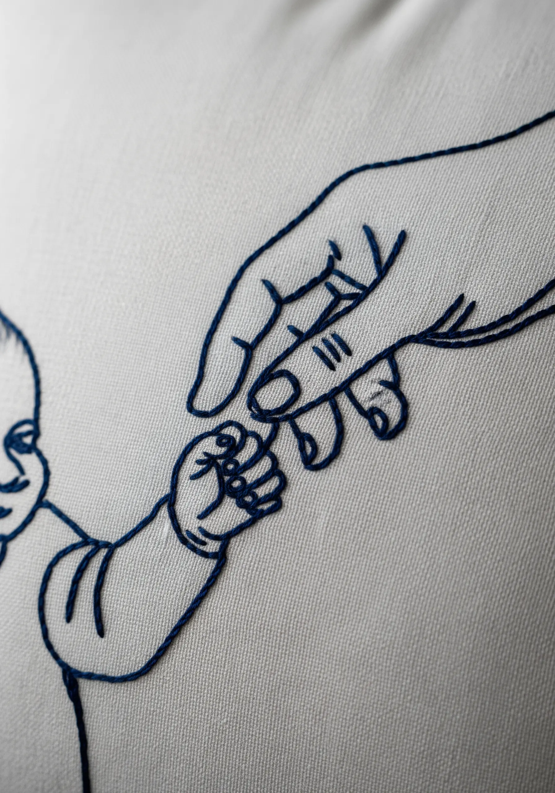 Close-up of a detailed line art embroidery showing a parent's hand holding a baby's hand.