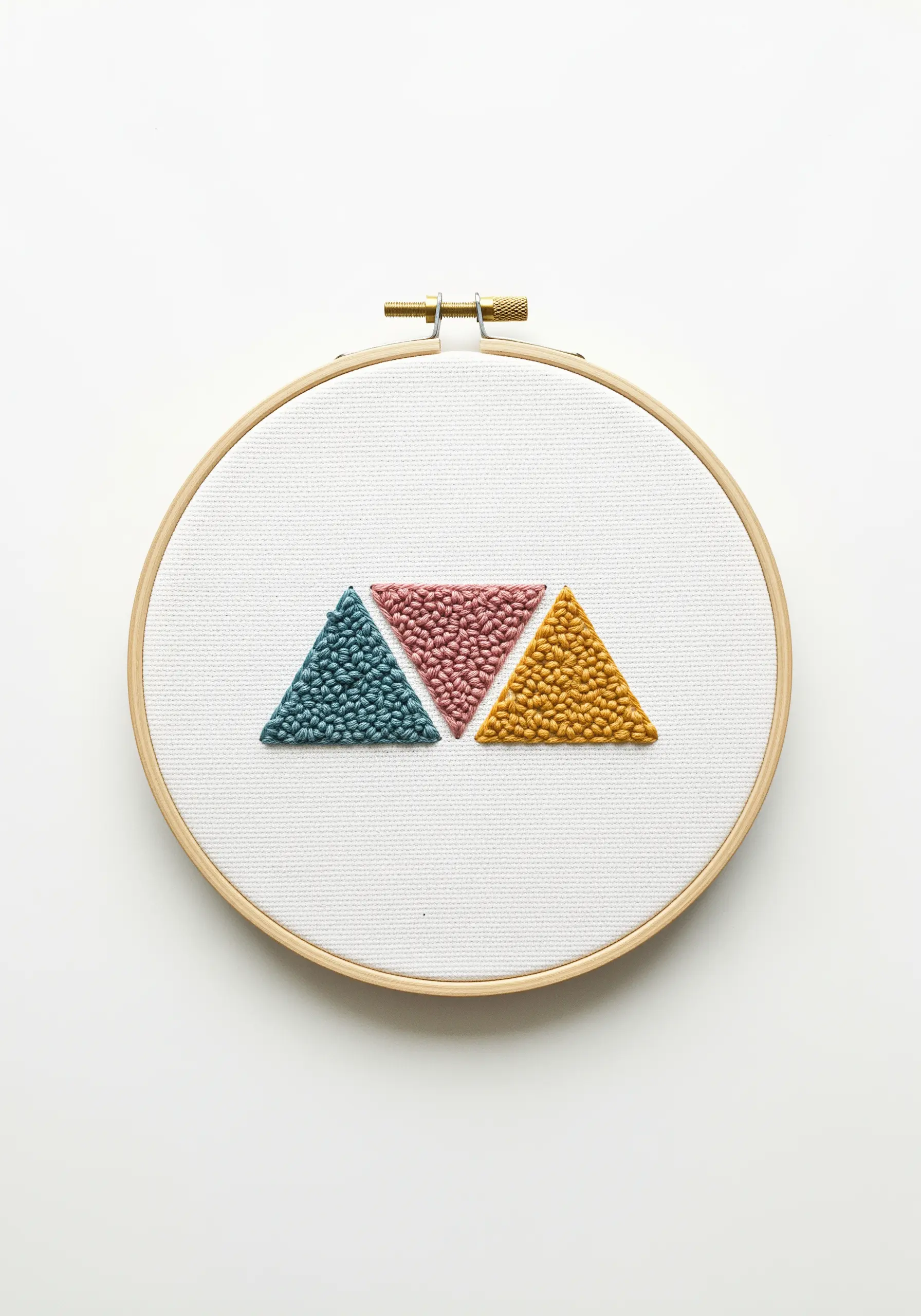 Three triangles filled with a dense, textured stitch resembling punch needle in teal, pink, and gold.