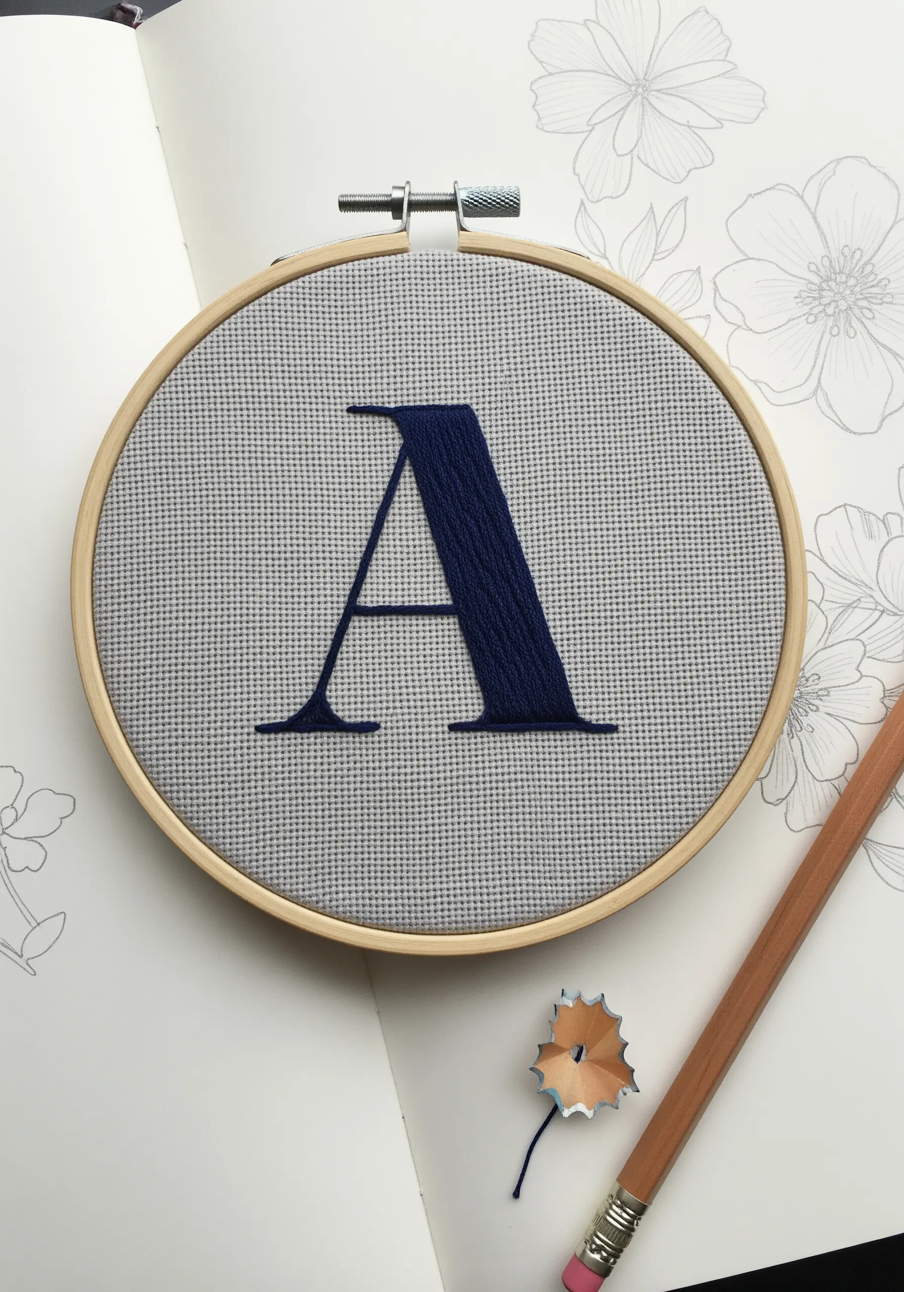 A perfectly embroidered serif letter 'A' in navy blue on gray Aida cloth.