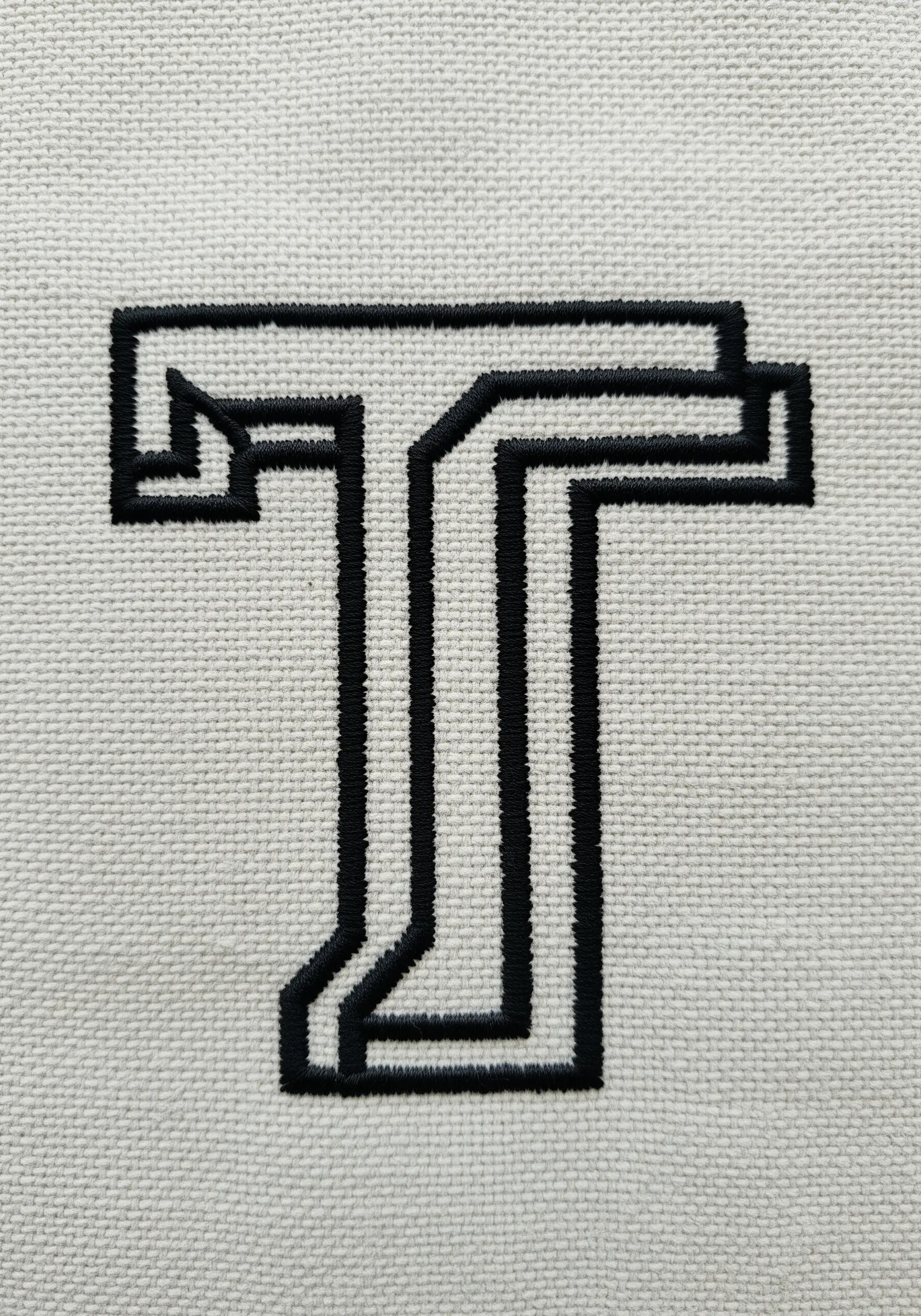 Modern, graphic letter 'T' embroidered with parallel black lines on white fabric.
