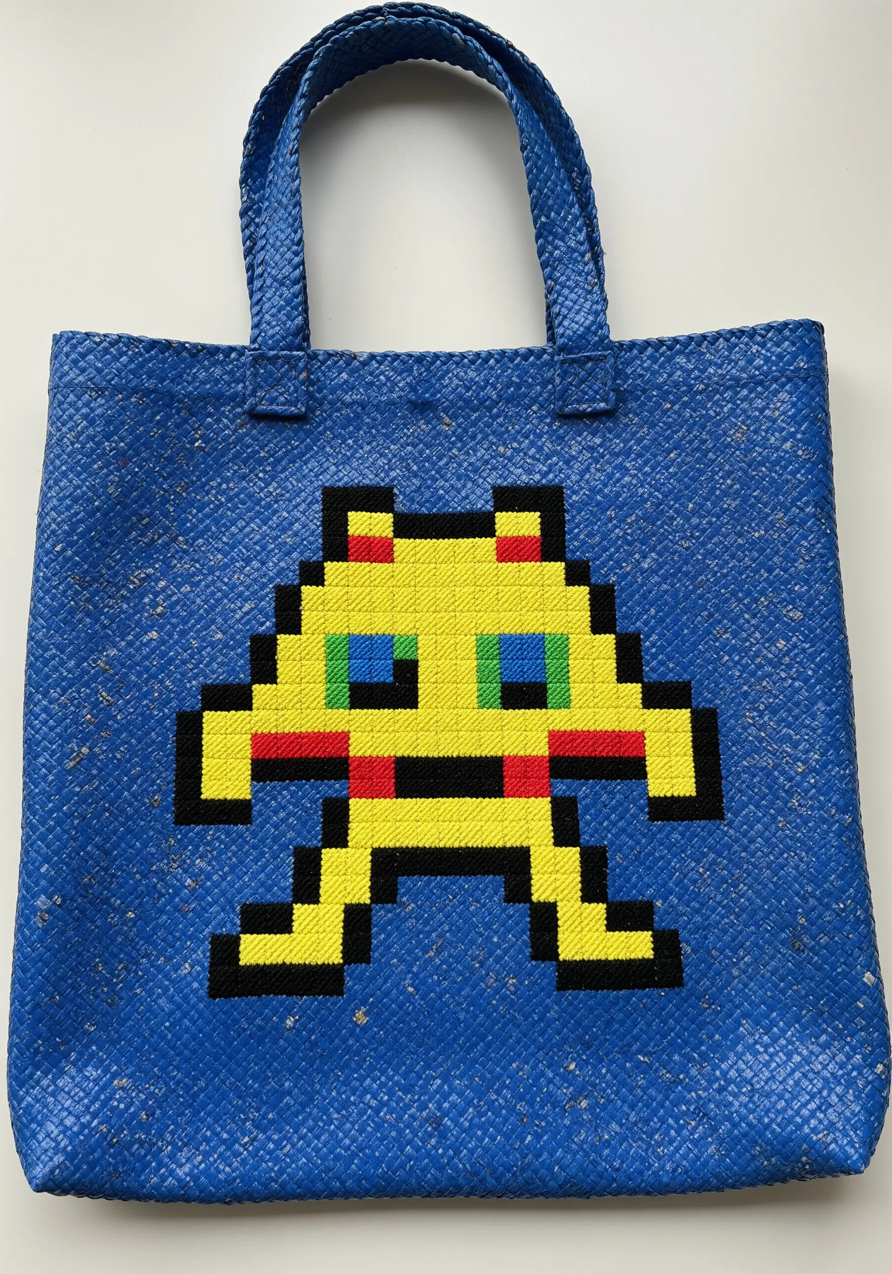 A pixelated video game character embroidered on a blue woven tote bag.