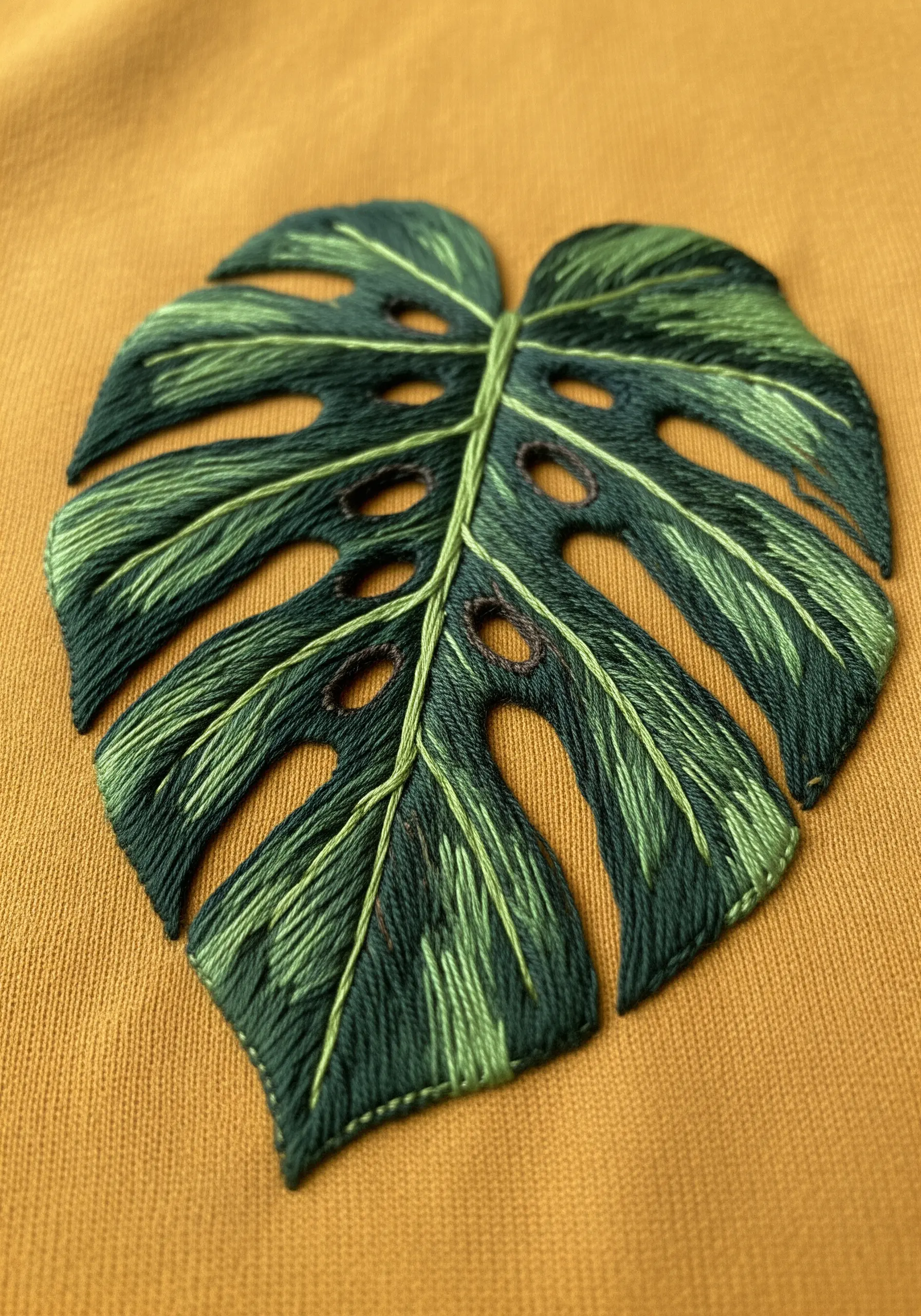 A close-up of an embroidered monstera leaf on a yellow jersey t-shirt.