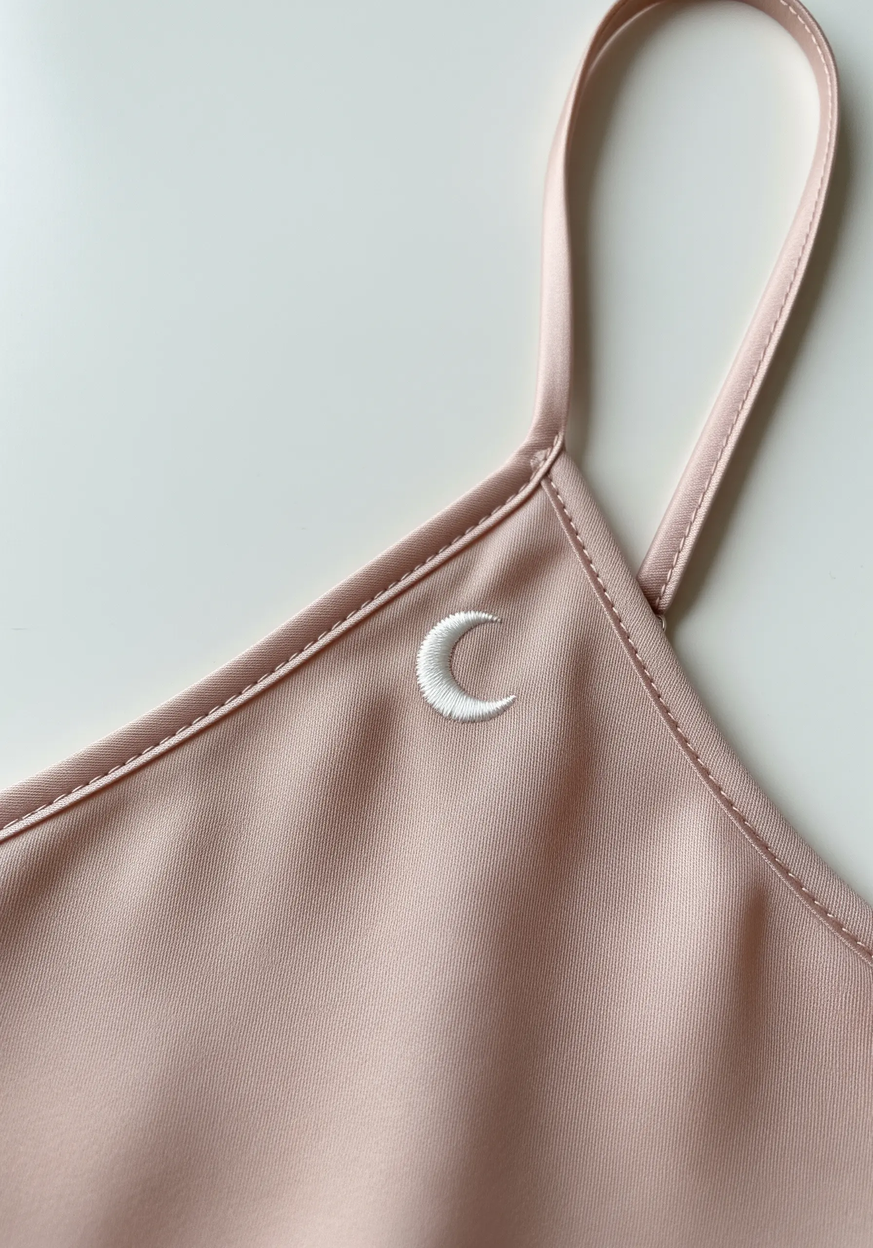 A small, white embroidered crescent moon on the satin strap of a blush pink top.