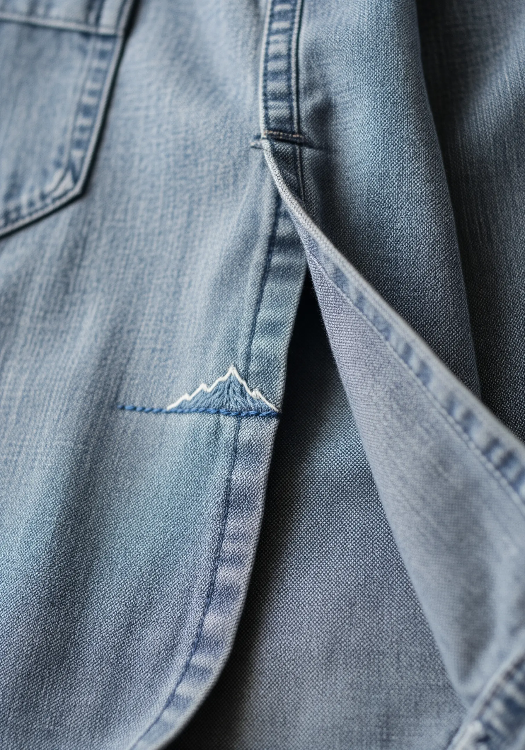 A small mountain range with white peaks embroidered on the side vent of a denim shirt.
