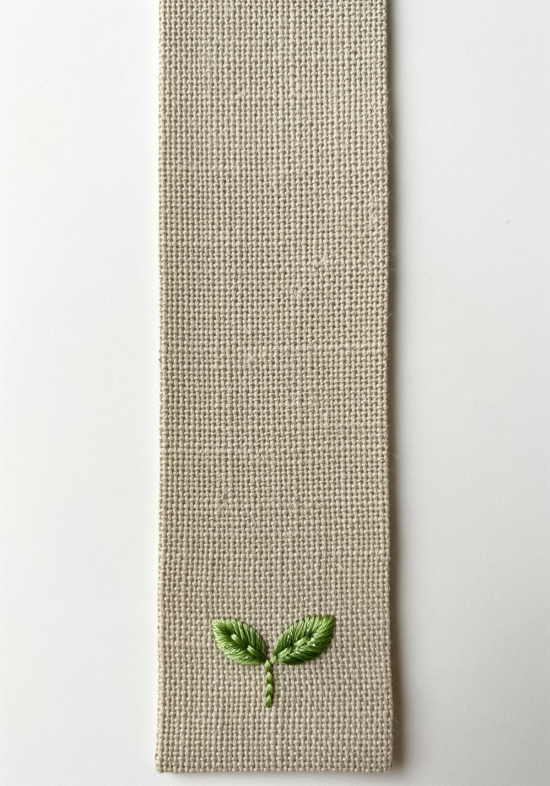 A tiny embroidered green seedling with two leaves at the bottom of a burlap bookmark.