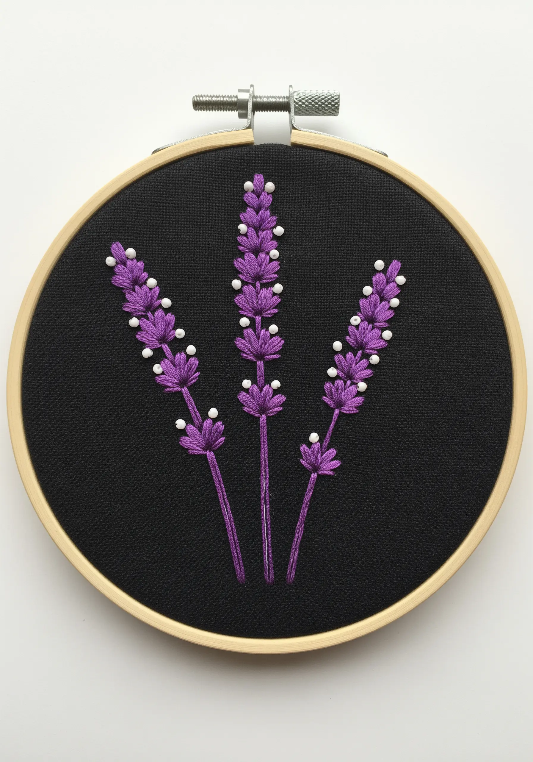 Three lavender stalks embroidered in purple with white beads on black fabric.