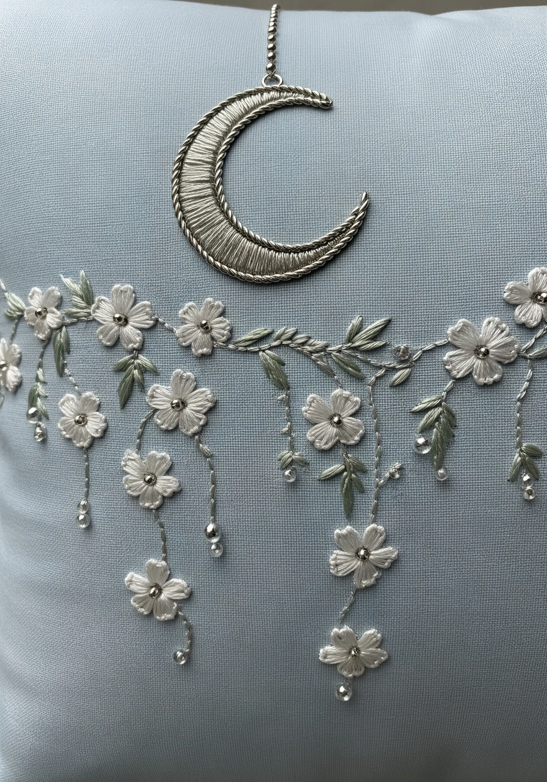 Cascading white flowers with silver thread and beads on a blue pillow.