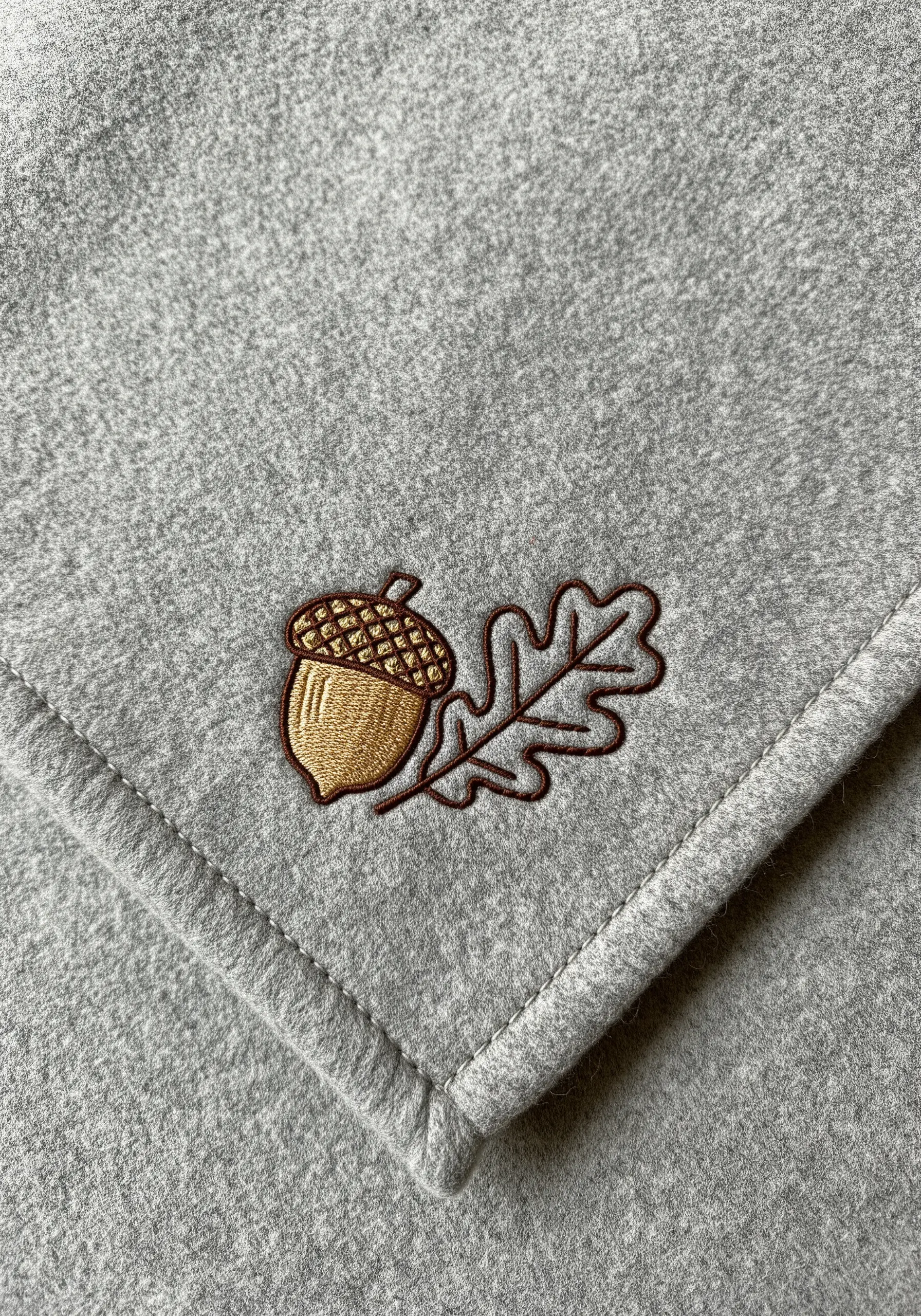 An embroidered acorn on grey fleece, with a textured cap and satin stitch body.