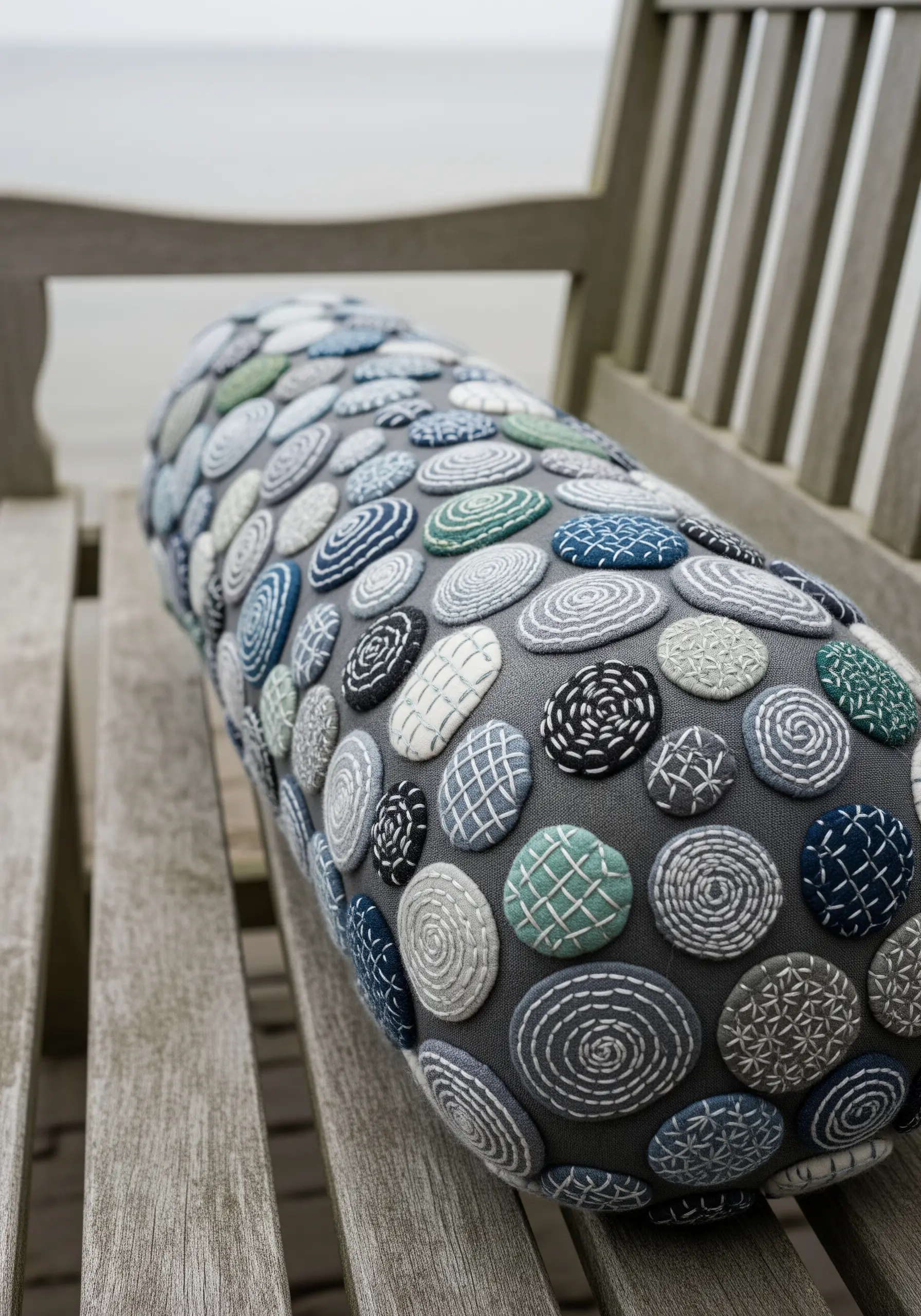 A bolster pillow covered in appliquéd fabric circles, each embroidered with a different pattern.