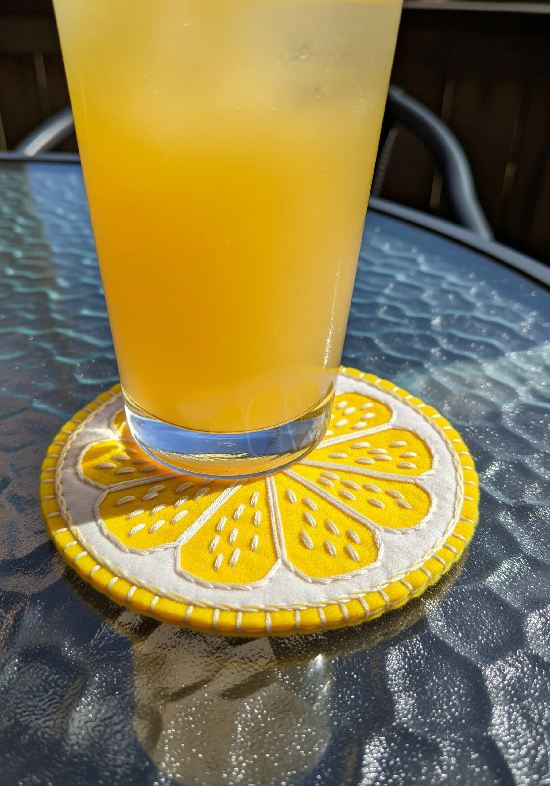 A round coaster designed like a lemon slice, made from felt with white embroidery details.