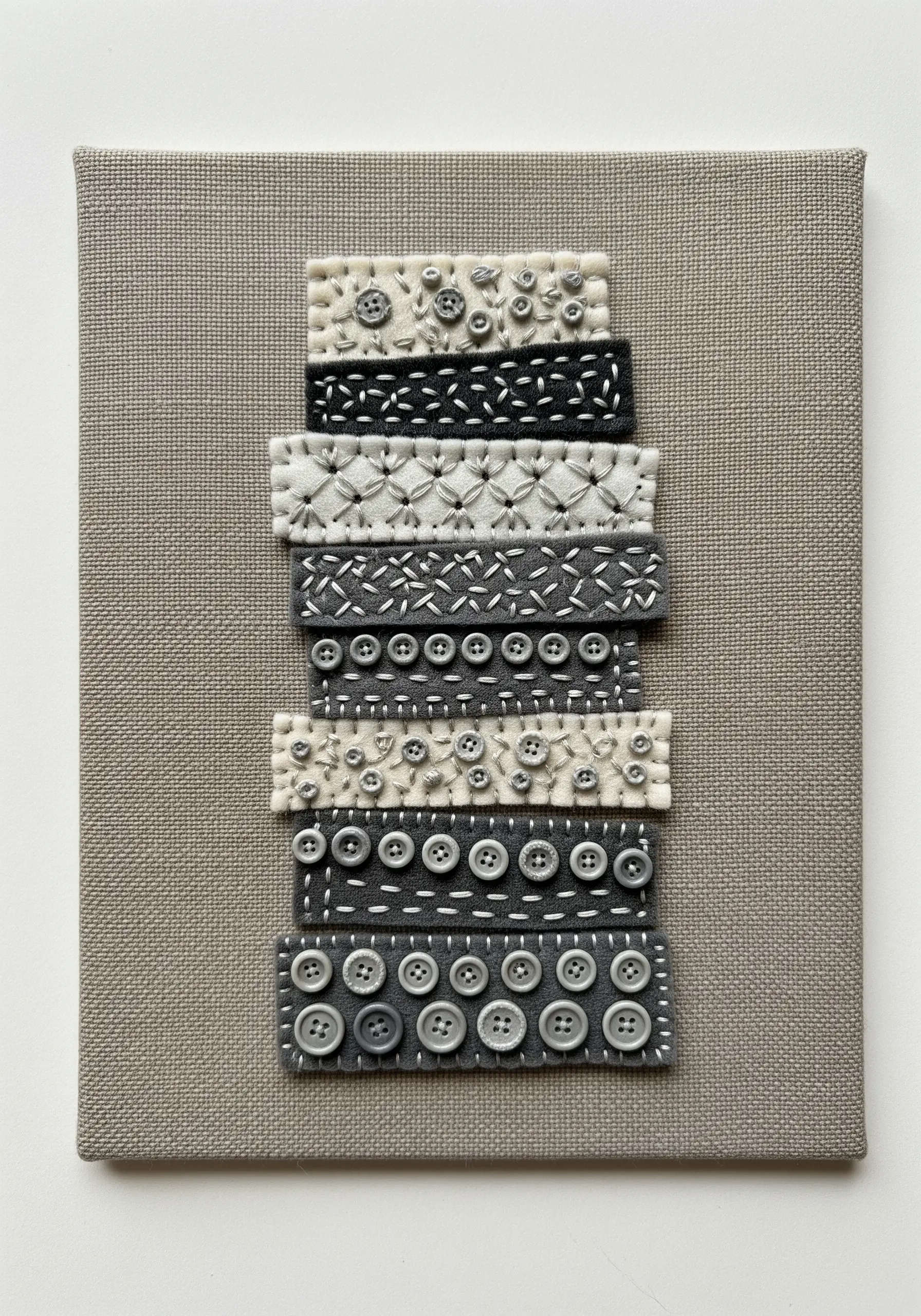 A textural sampler made of felt strips decorated with different stitches and gray buttons.