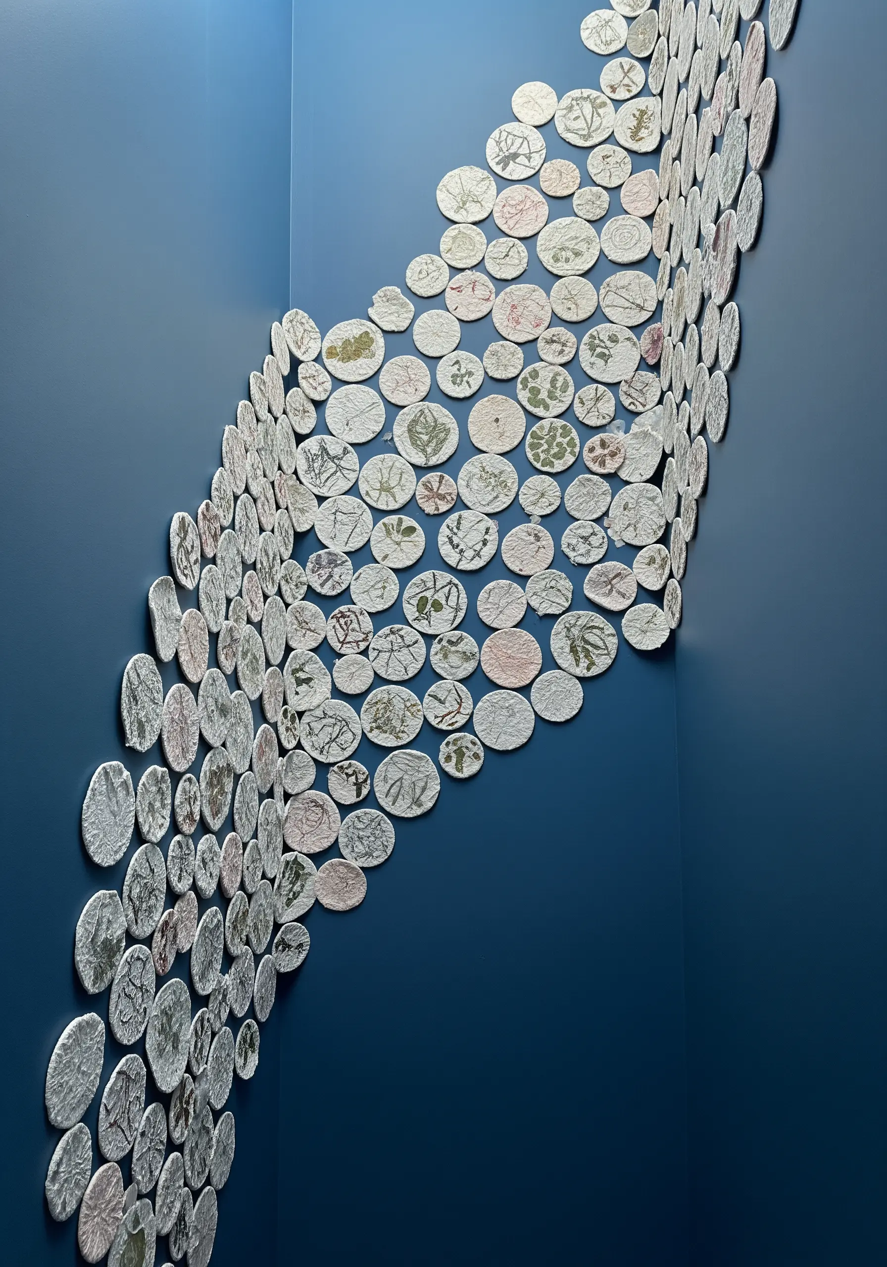 A wall installation made of many small, circular pieces of paper with botanical prints, arranged in a wave.
