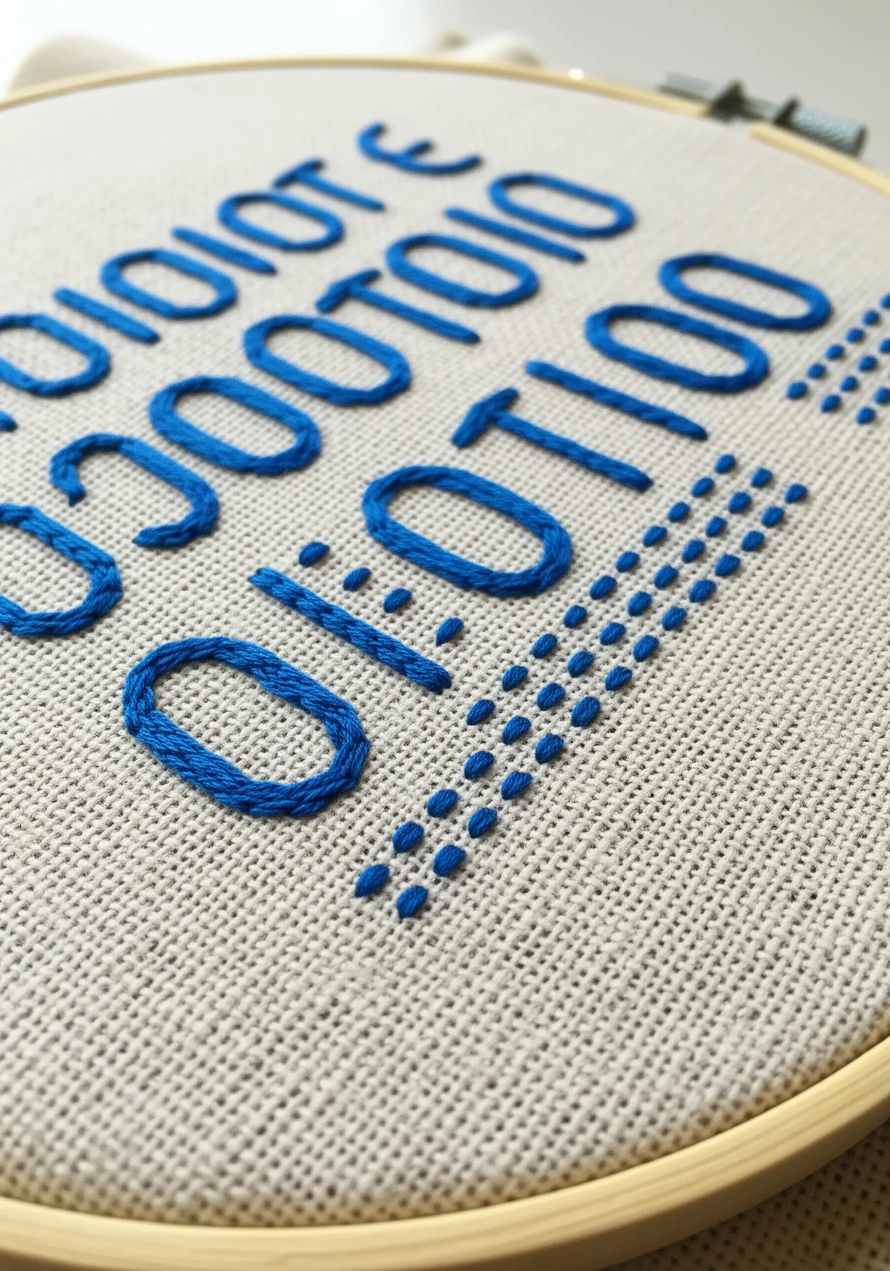 Close-up of embroidered binary code in blue thread on neutral linen-like fabric.