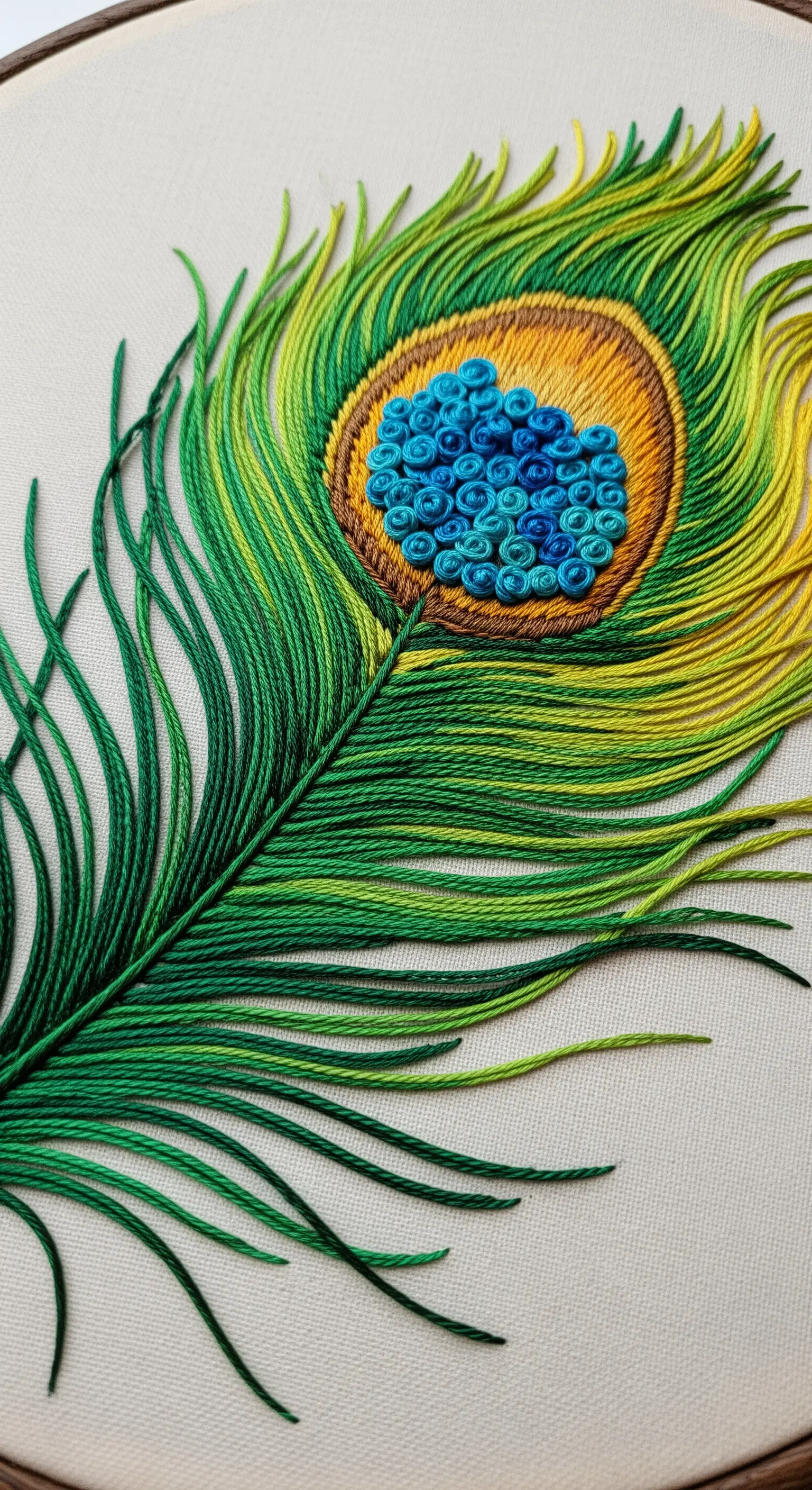 Close-up of an embroidered peacock feather using thread painting and blue French knots.