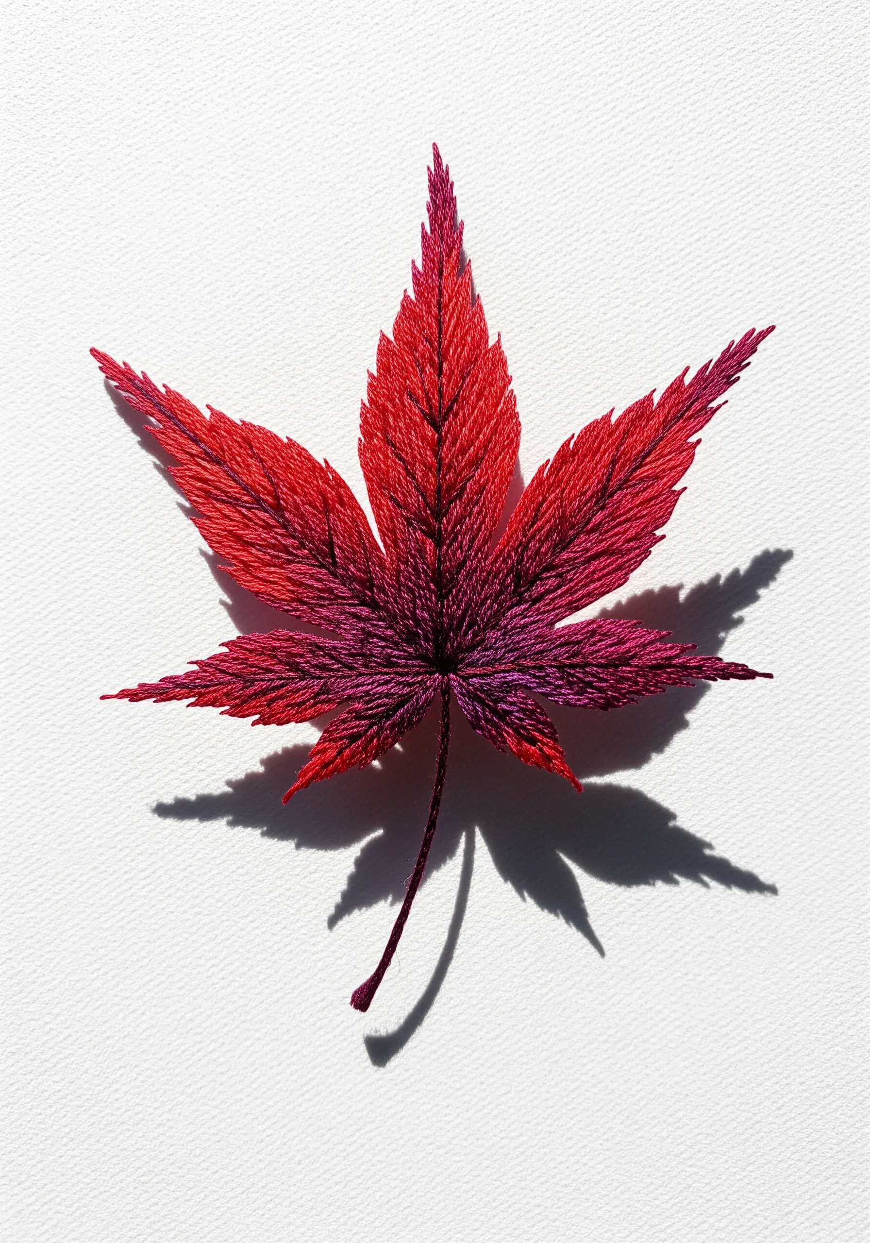 A Japanese maple leaf embroidered with thread painting, blending from red to deep purple.