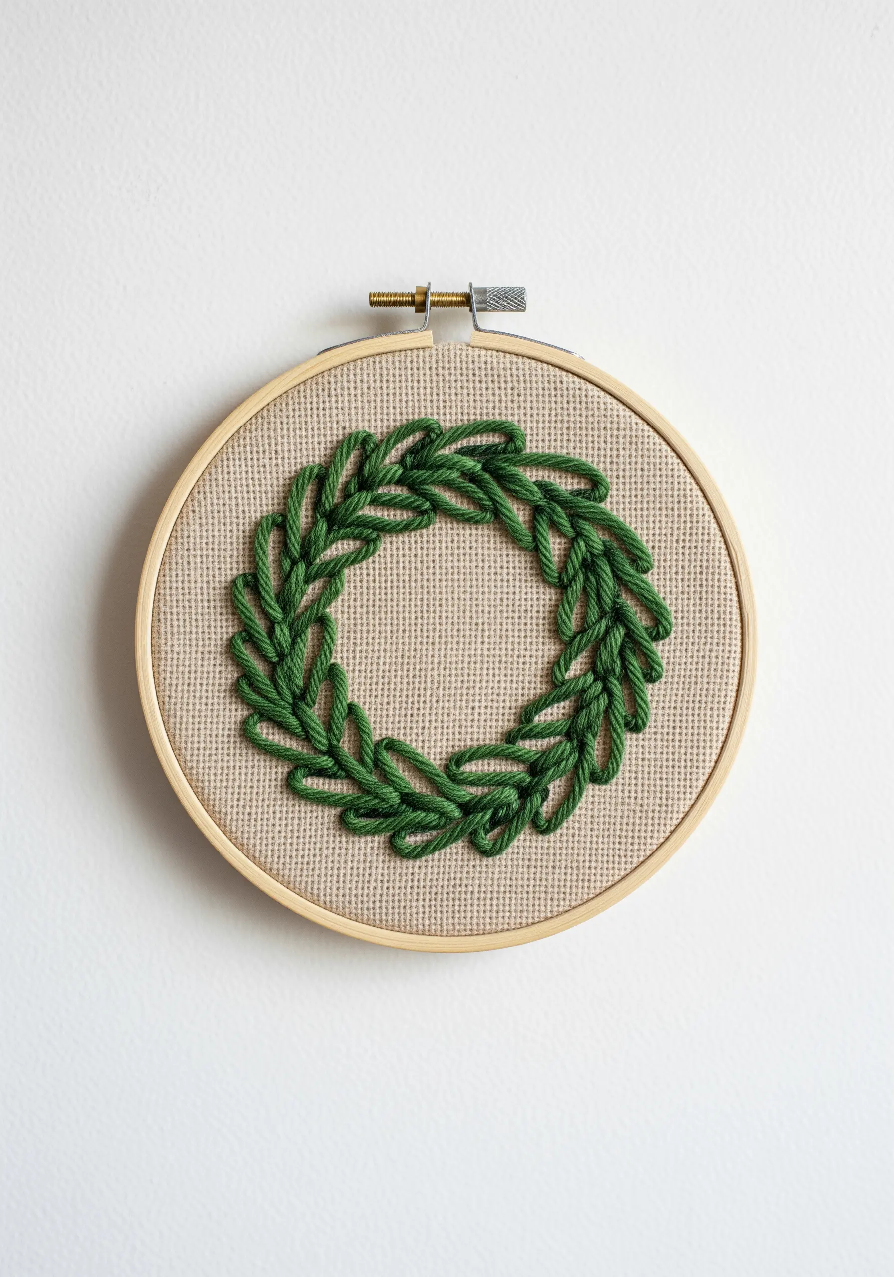 A dimensional green wreath made from raised chain stitch in an embroidery hoop.