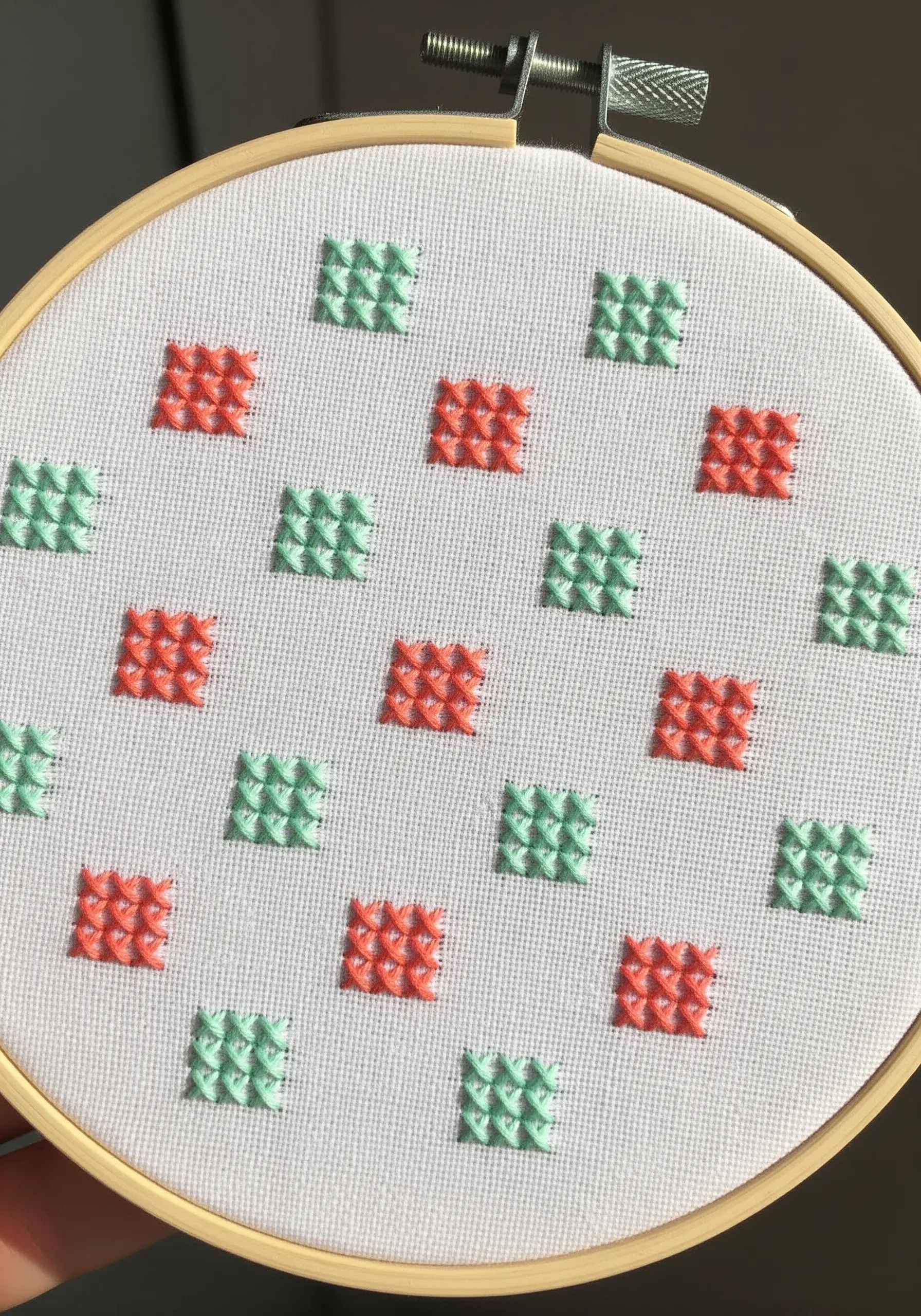 A grid pattern of small, raised woven stitches in alternating coral and mint green.