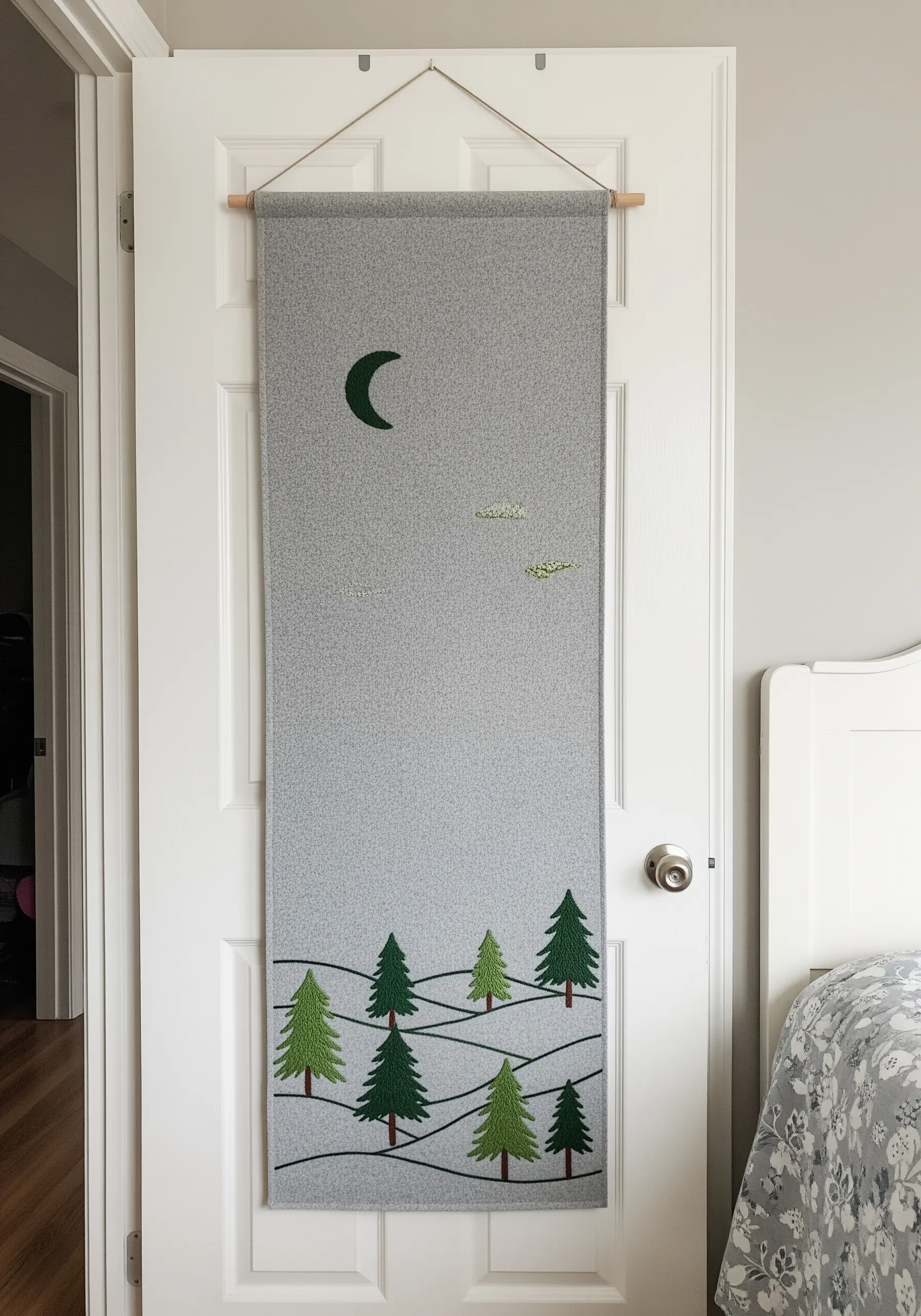 A long grey wall hanging with a felt appliqué scene of green pine trees.