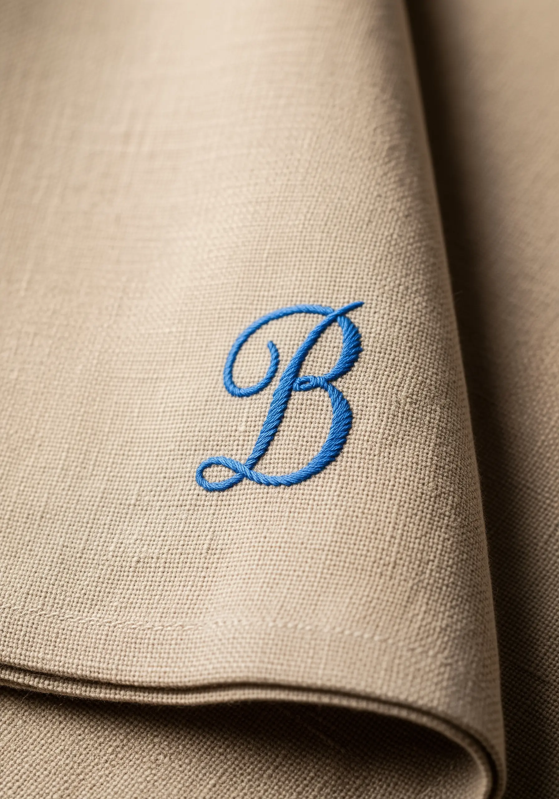 A dimensional blue embroidered 'B' monogram on a beige linen napkin.