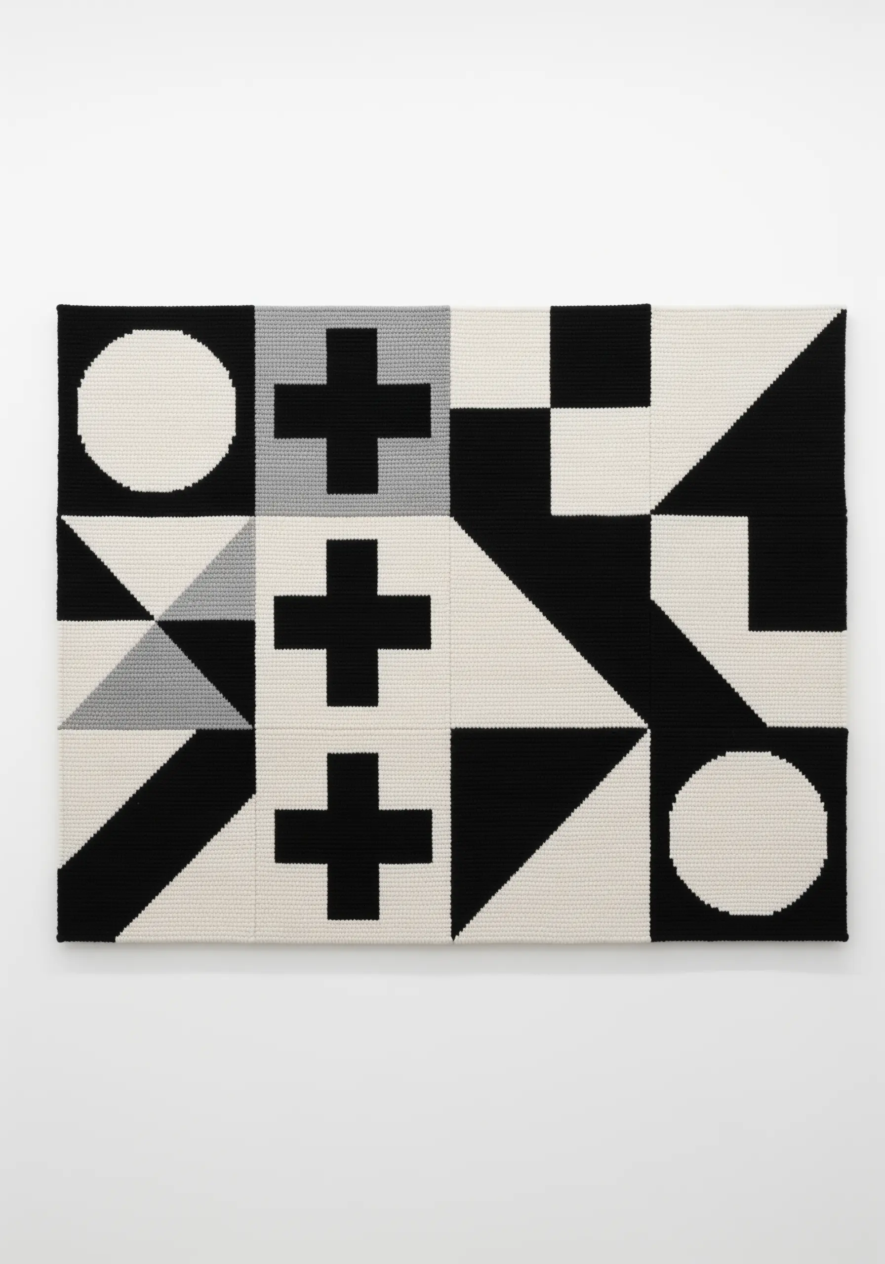 A black, white, and gray tapestry with a modular pattern of geometric shapes like crosses and circles.