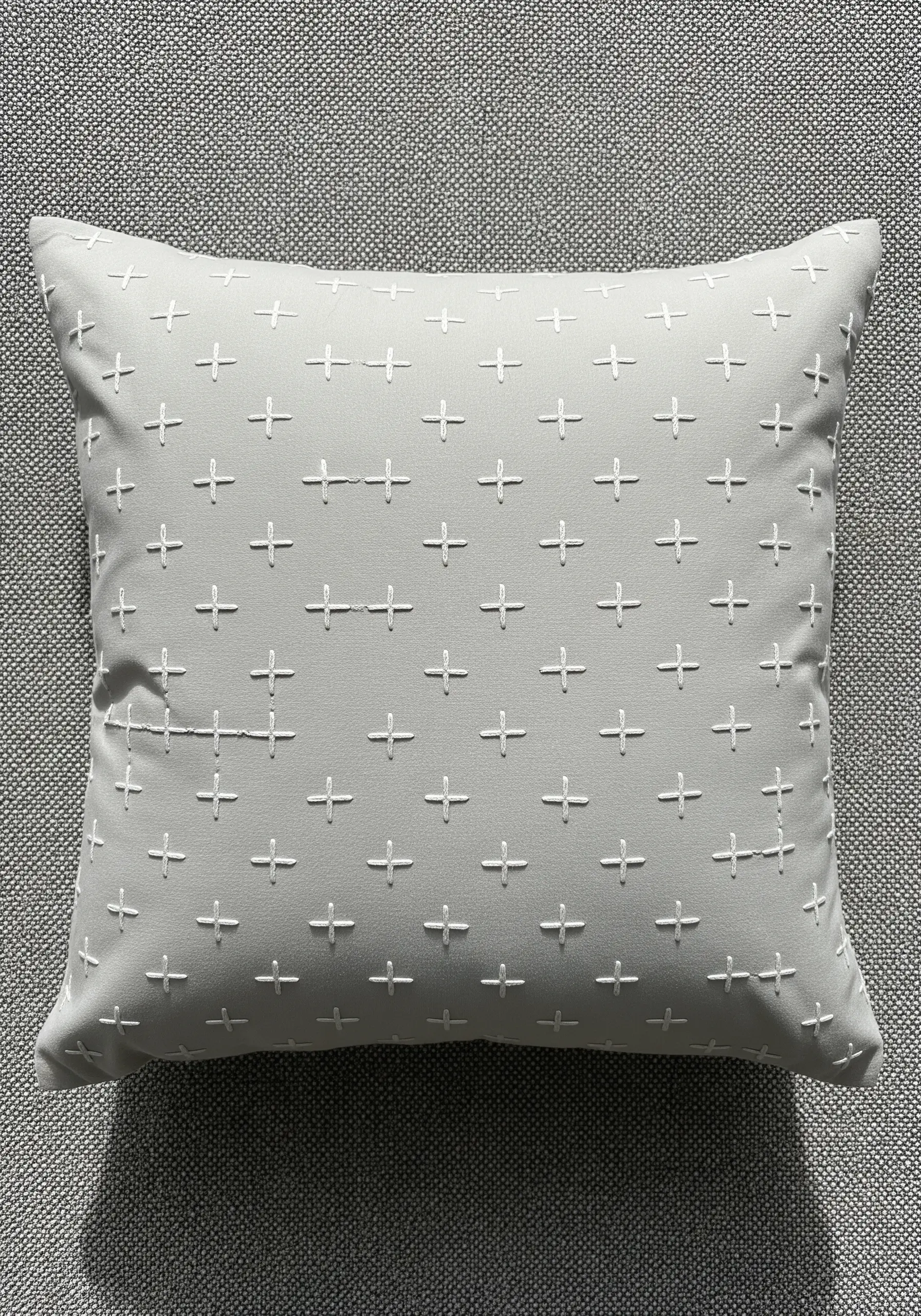 A repeating pattern of small white plus signs meticulously stitched onto a light grey pillow.
