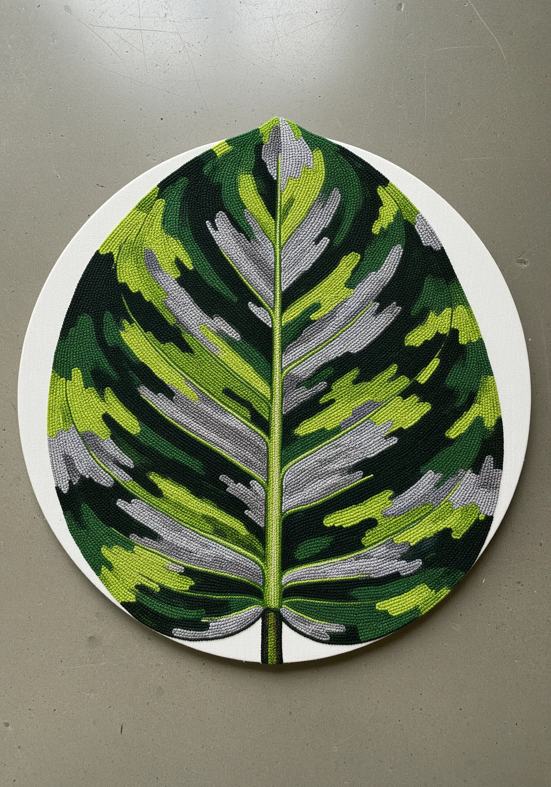 A graphic Calathea leaf with chunky, textured stitches in green and grey on a round canvas.