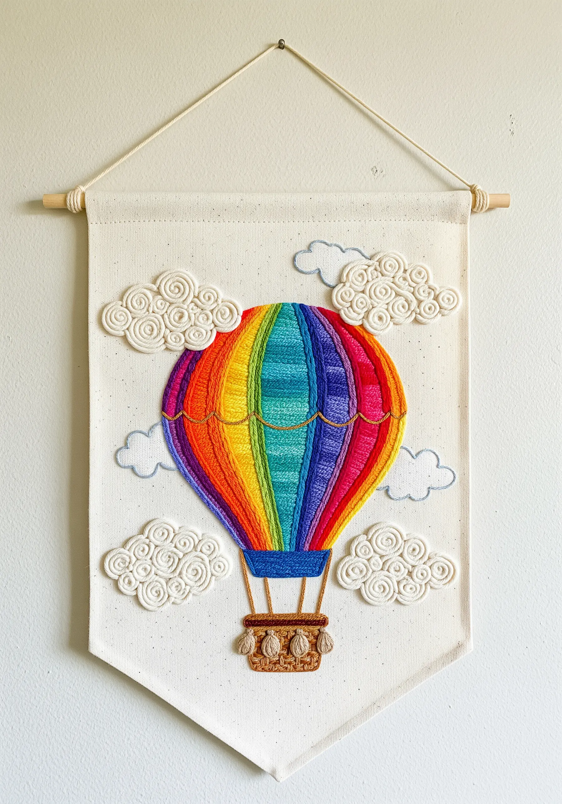 A wall hanging with a rainbow hot air balloon and fluffy, three-dimensional clouds.