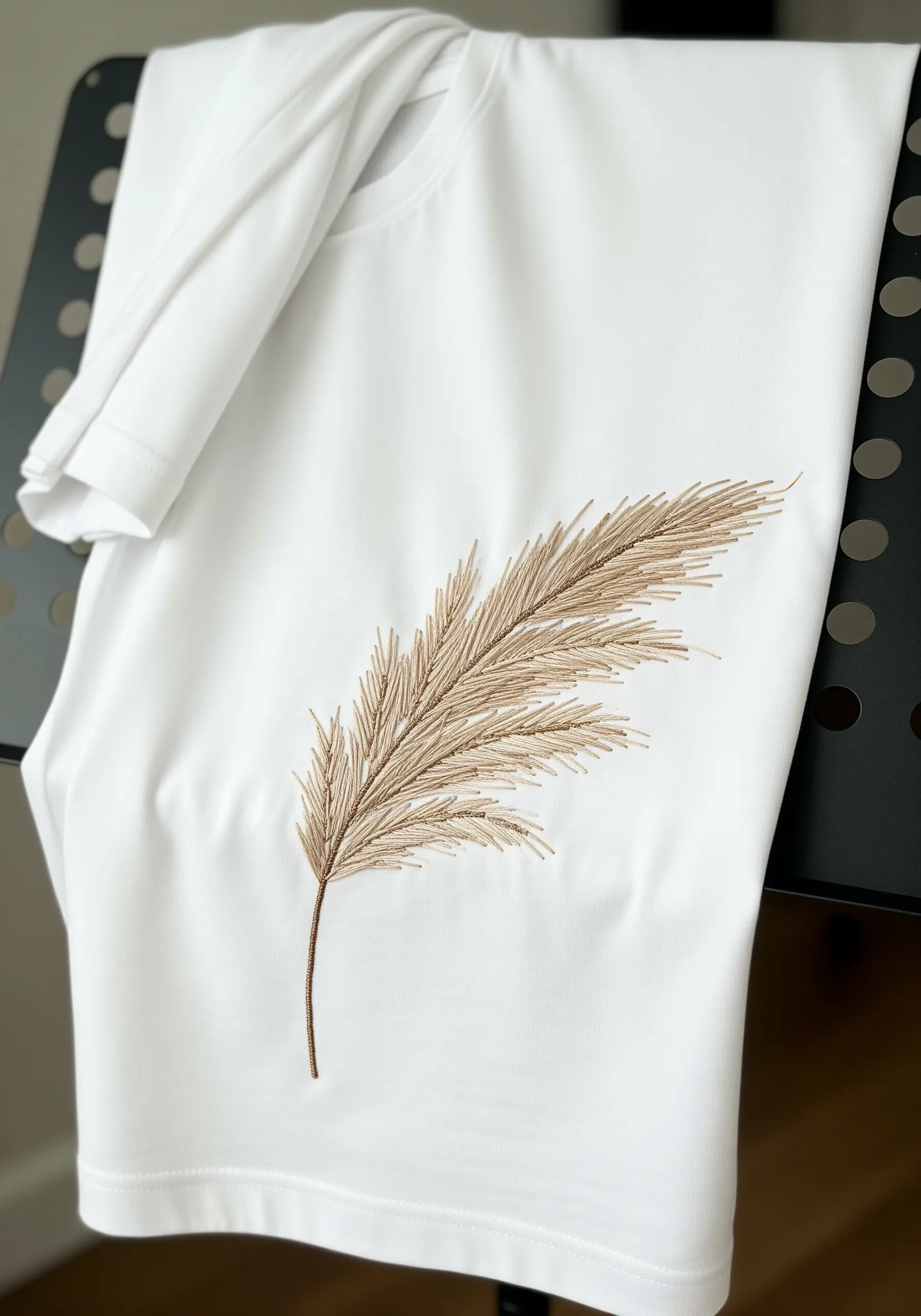 A plume of pampas grass embroidered in beige tones on a white t-shirt.