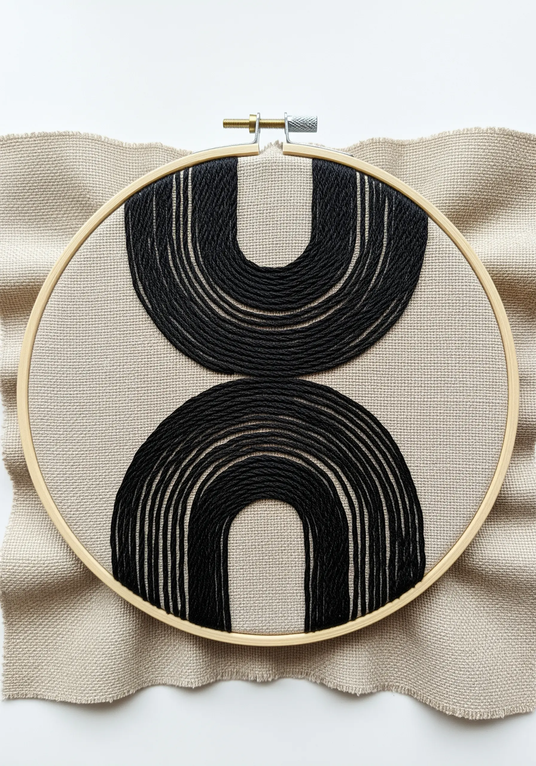 Abstract black yarn embroidery with symmetrical arches on beige fabric in a wooden hoop.